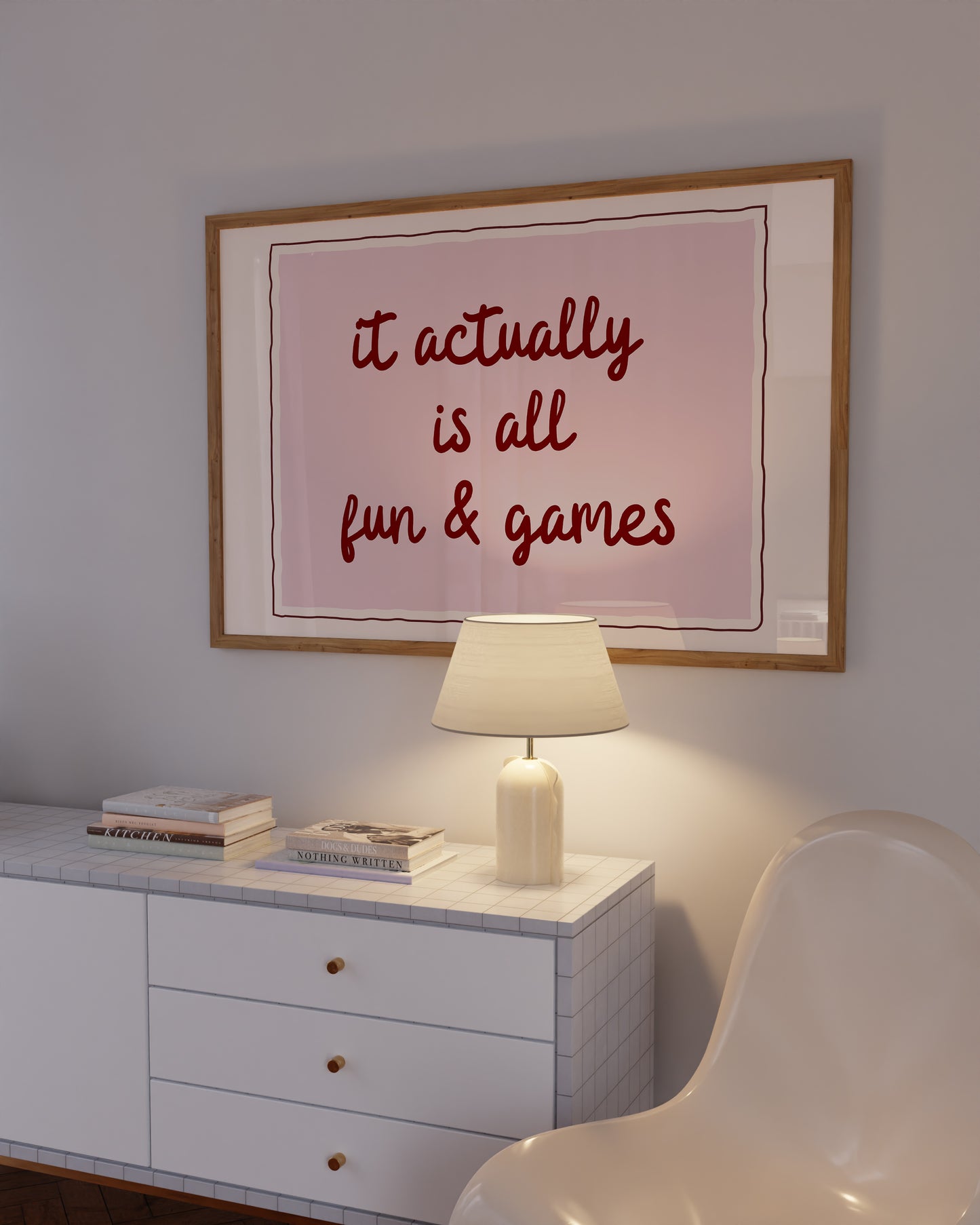 Horizontal wall print with a soft pink centre panel and white border with dark red scalloped outline, bold dark red cursive script reading it actually is all fun & games