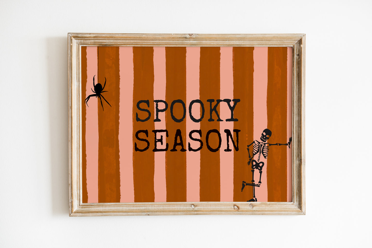 Horizontal print with orange and pink hand-painted vertical stripes, the words "SPOOKY SEASON" in bold black typewriter-style letters, a hanging black spider on the left, and a dancing skeleton illustration on the right.