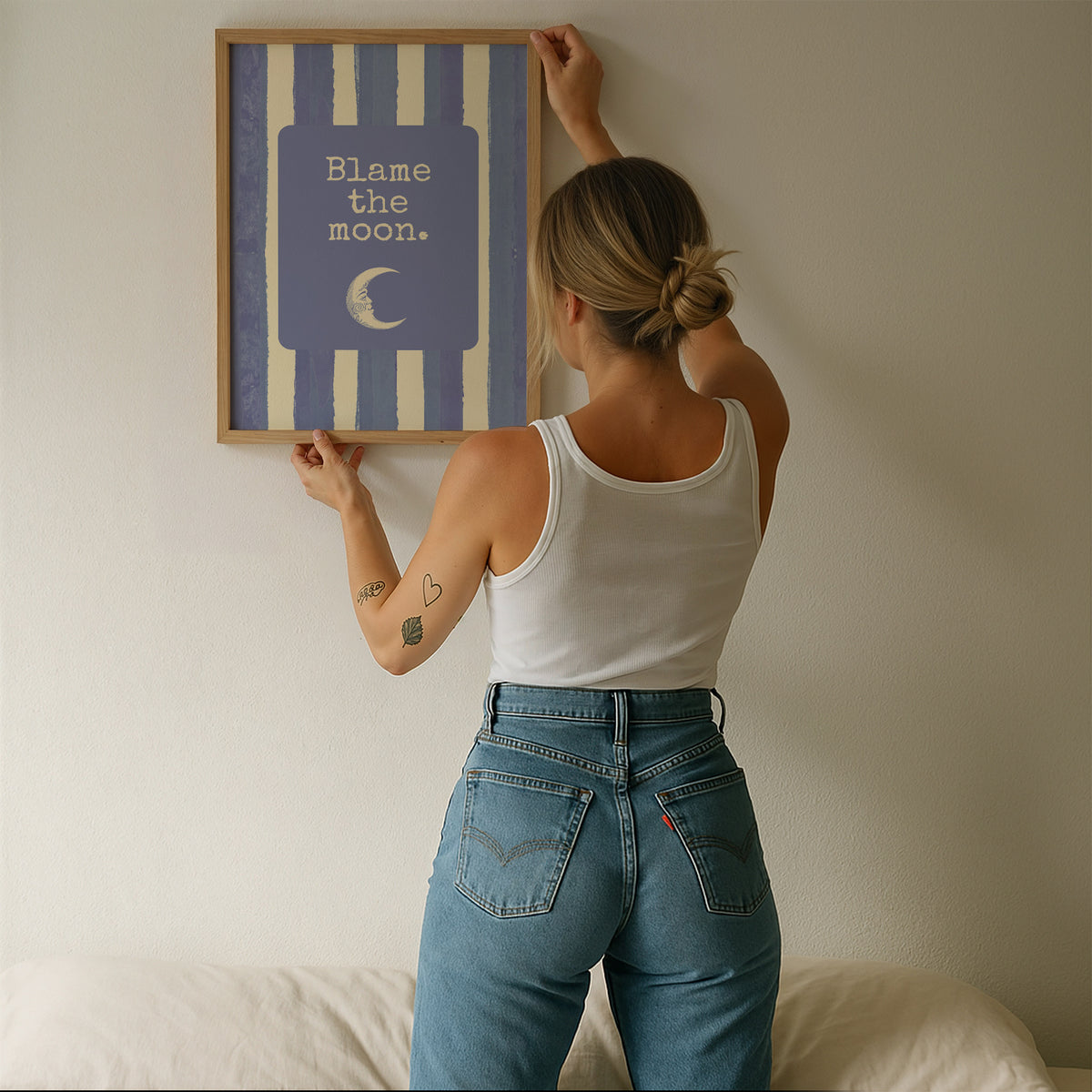 Portrait digital print with blue-and-cream striped background featuring a rounded blue panel with the text "Blame the moon." in cream lettering above a vintage-style crescent moon face illustration.