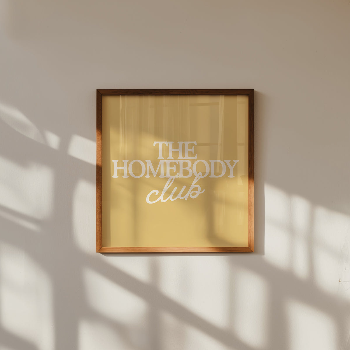 Square digital print with a mustard yellow background featuring "THE HOMEBODY" in bold cream serif type stacked above "club" in cream cursive script, centered typography layout.
