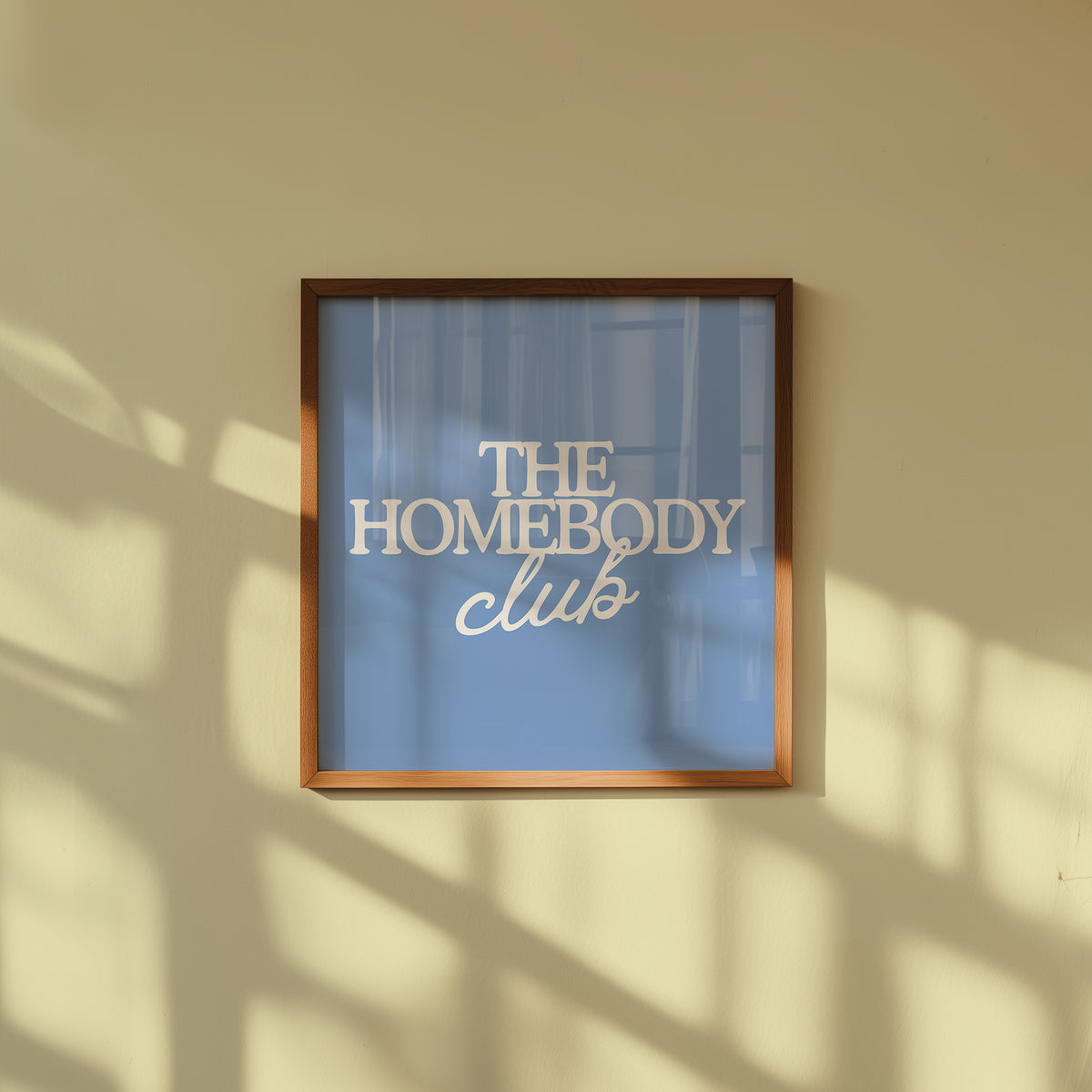 Square digital print with a dusty blue background featuring "THE HOMEBODY" in bold cream serif type stacked above "club" in cream cursive script, centered typography layout.
