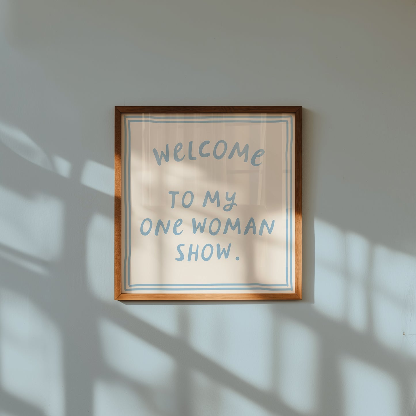 Beige print with dusty blue hand-lettered text "Welcome to my one woman show." inside a double-line border