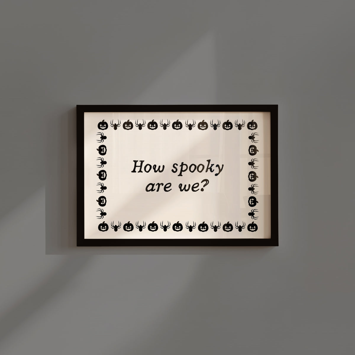 Landscape digital print with a cream background bordered by alternating black pumpkin and spider illustrations, framing the hand-lettered phrase "How spooky are we?" in black script.