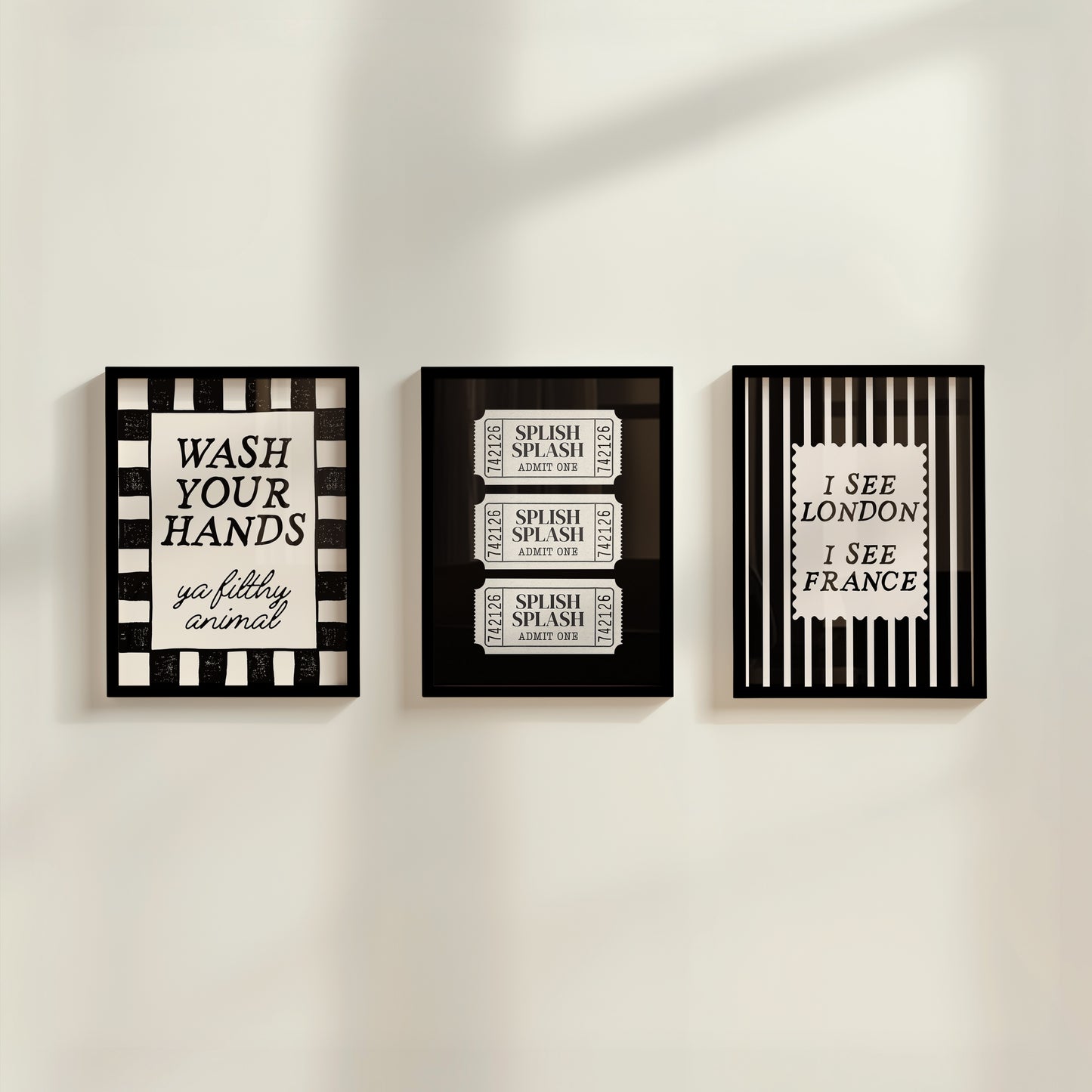 Set of 3 black and white bathroom prints: "Wash your hands ya filthy animal" in black cursive bordered by a black and white checkered frame, three black ticket-stub illustrations reading "Splish Splash, Admit One," and "I See London I See France" in a scalloped stamp frame on black and white stripes.