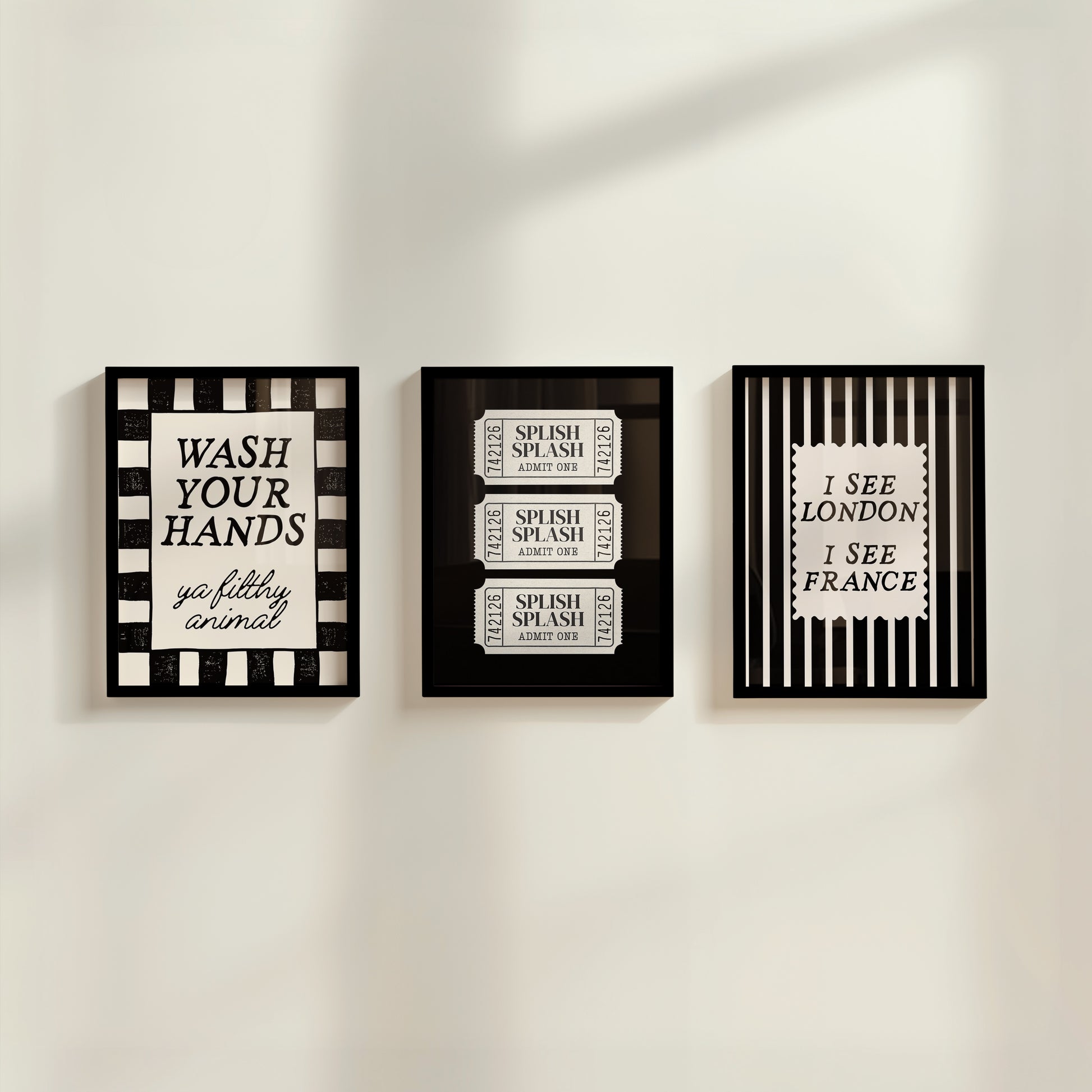 Set of 3 black and white bathroom prints: "Wash your hands ya filthy animal" in black cursive bordered by a black and white checkered frame, three black ticket-stub illustrations reading "Splish Splash, Admit One," and "I See London I See France" in a scalloped stamp frame on black and white stripes.