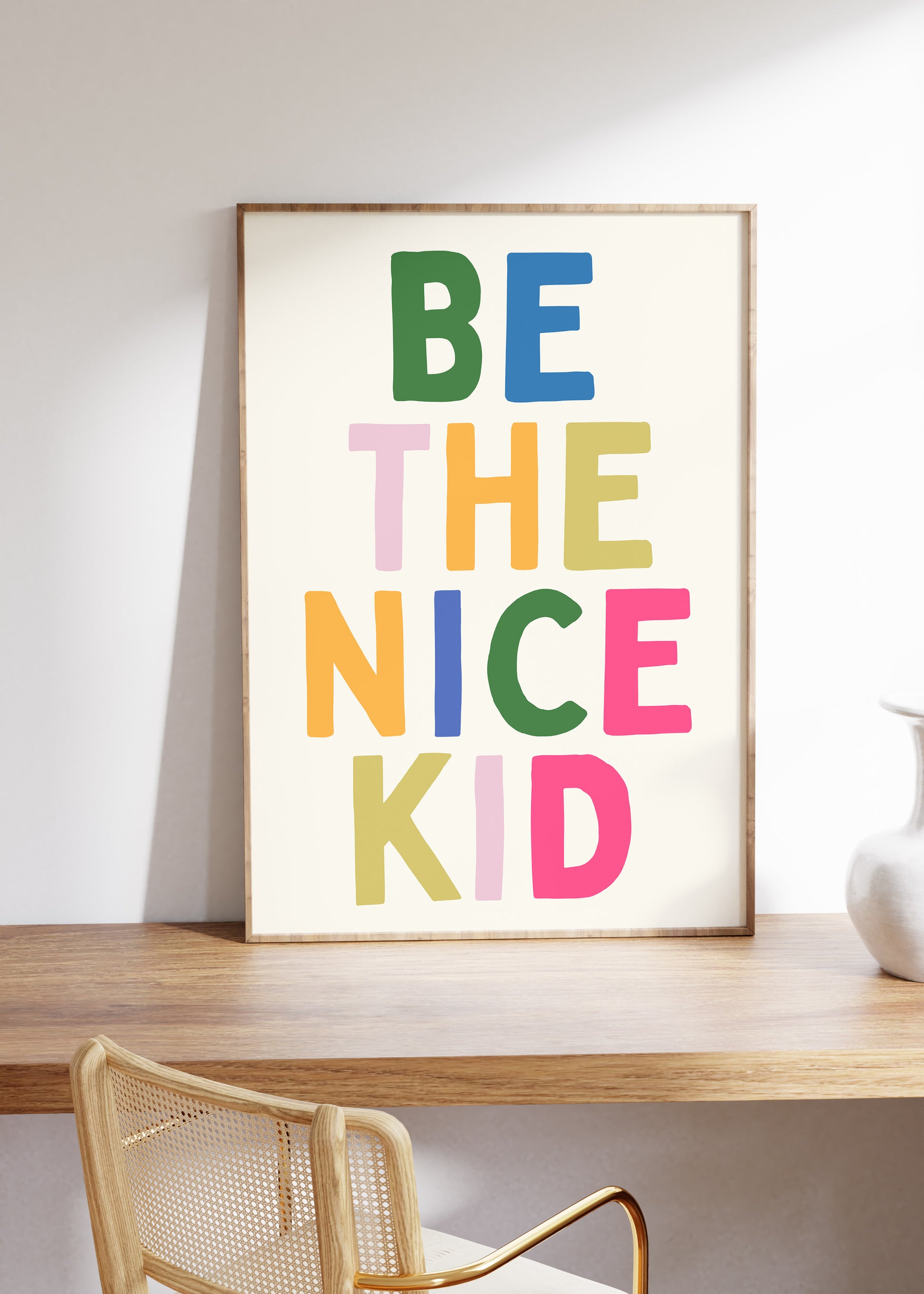 Vertical print with the words "BE THE NICE KID" stacked in large multicolored bubble letters on a cream background in a blue frame.