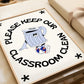 Vertical cream wall print with bold arched black typography reading Please Keep Our Classroom Clean surrounding a retro cartoon trash can character wearing sneakers with asterisk corner details