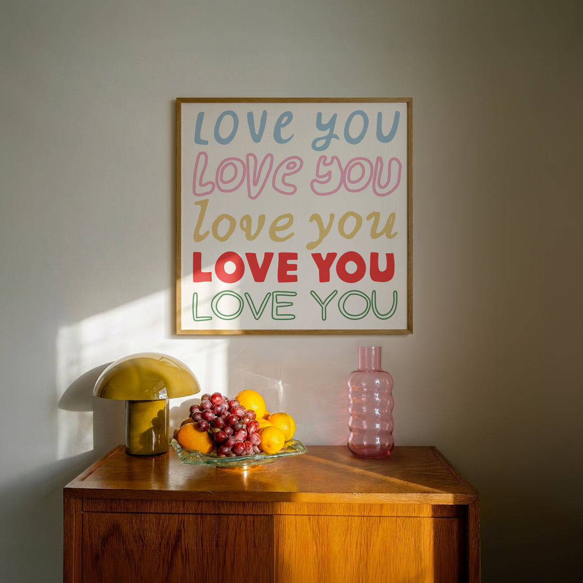 Square print with the words "Love You" repeated five times in different colors, fonts, and styles — blue, pink, gold, red, and green — stacked on a cream background.
