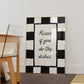 Black and white checkered print with a scalloped border and the handwritten quote "Kisses if you do the dishes" in black script