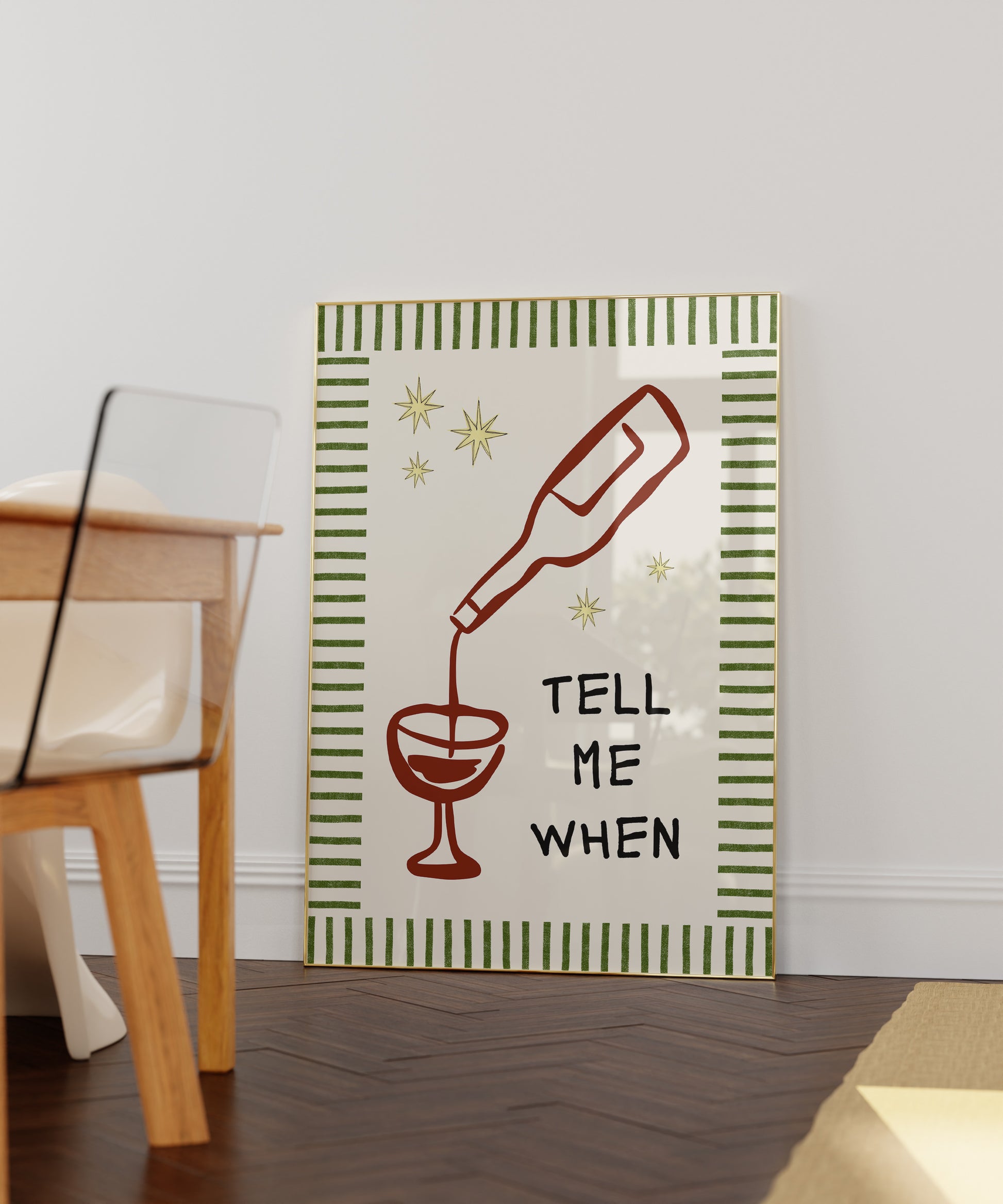 Vertical cream wall print with green stripe border, gold star details, and bold black typography reading Tell Me When alongside dark red hand-drawn line art of a wine bottle pouring into a glass