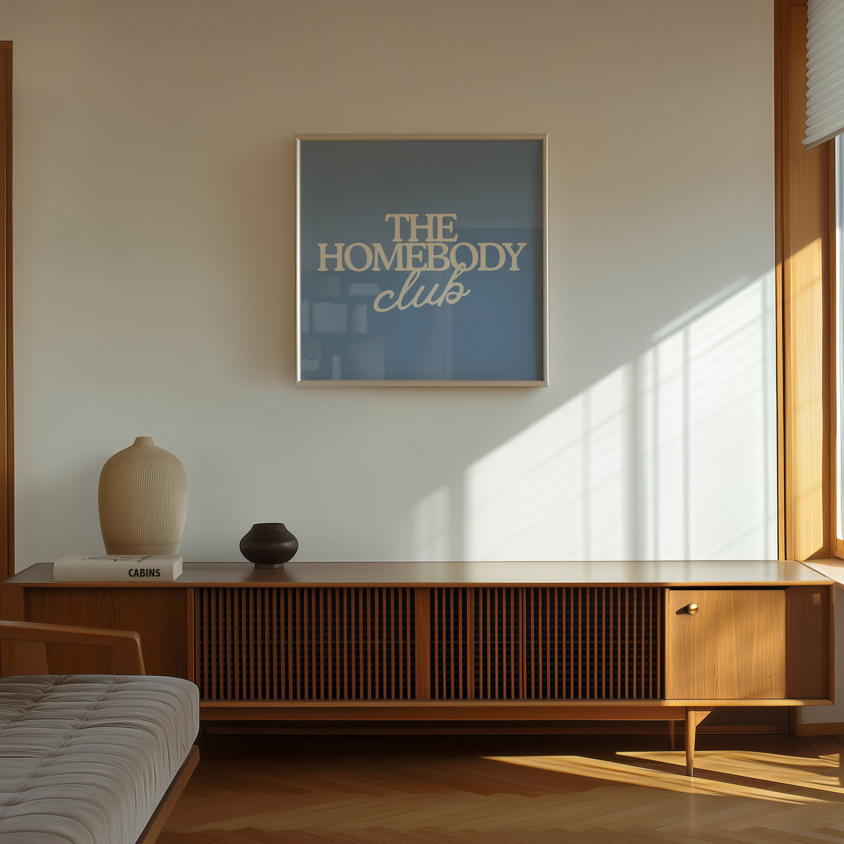 Square digital print with a dusty blue background featuring "THE HOMEBODY" in bold cream serif type stacked above "club" in cream cursive script, centered typography layout.