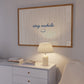 Horizontal print with thin hand-painted tan and cream vertical stripes, the quote "stay awhile" in navy cursive script, and a small hand-drawn smiley face beneath it.
