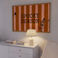 Horizontal print with orange and pink hand-painted vertical stripes, the words "SPOOKY SEASON" in bold black typewriter-style letters, a hanging black spider on the left, and a dancing skeleton illustration on the right.