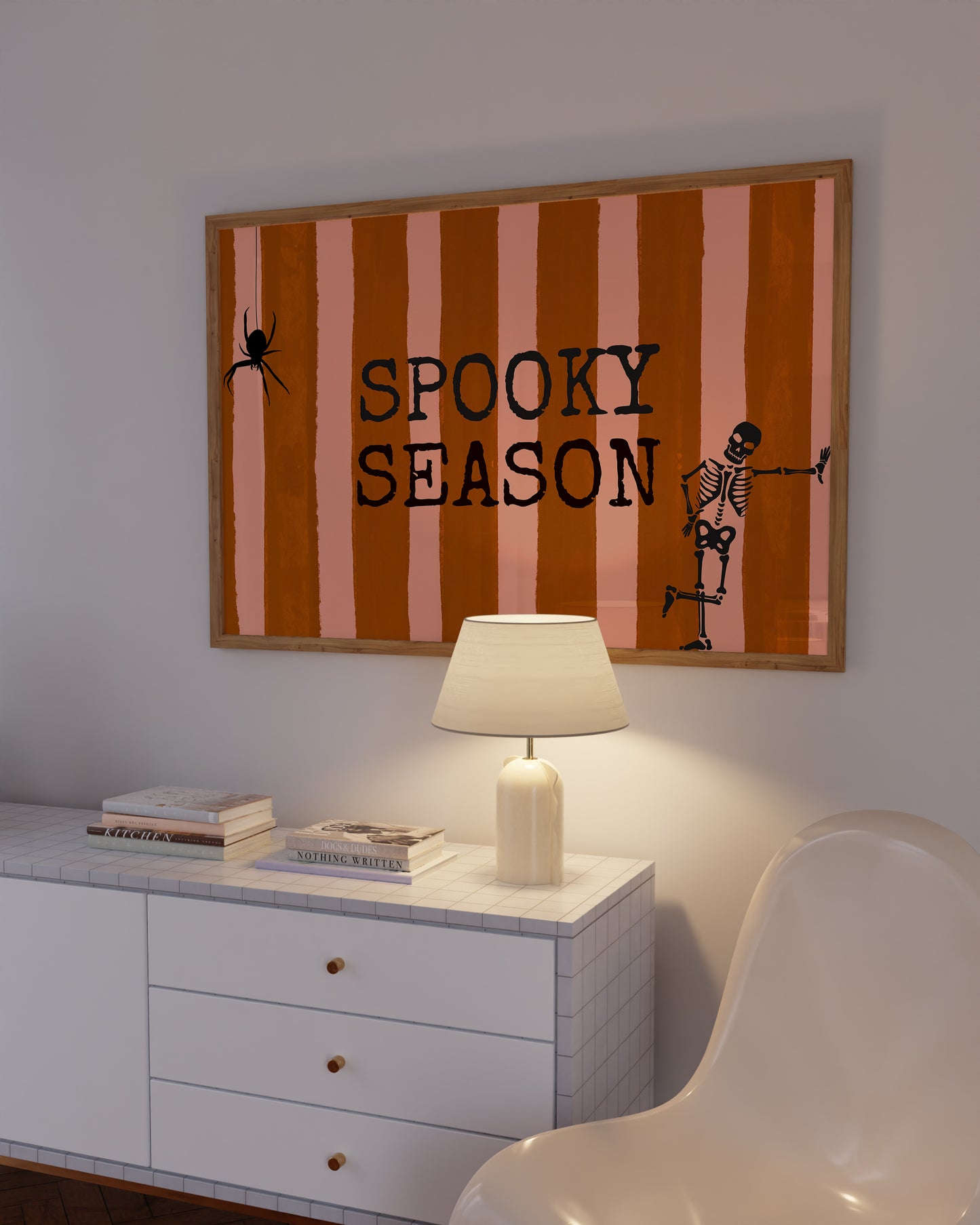 Horizontal print with orange and pink hand-painted vertical stripes, the words "SPOOKY SEASON" in bold black typewriter-style letters, a hanging black spider on the left, and a dancing skeleton illustration on the right.