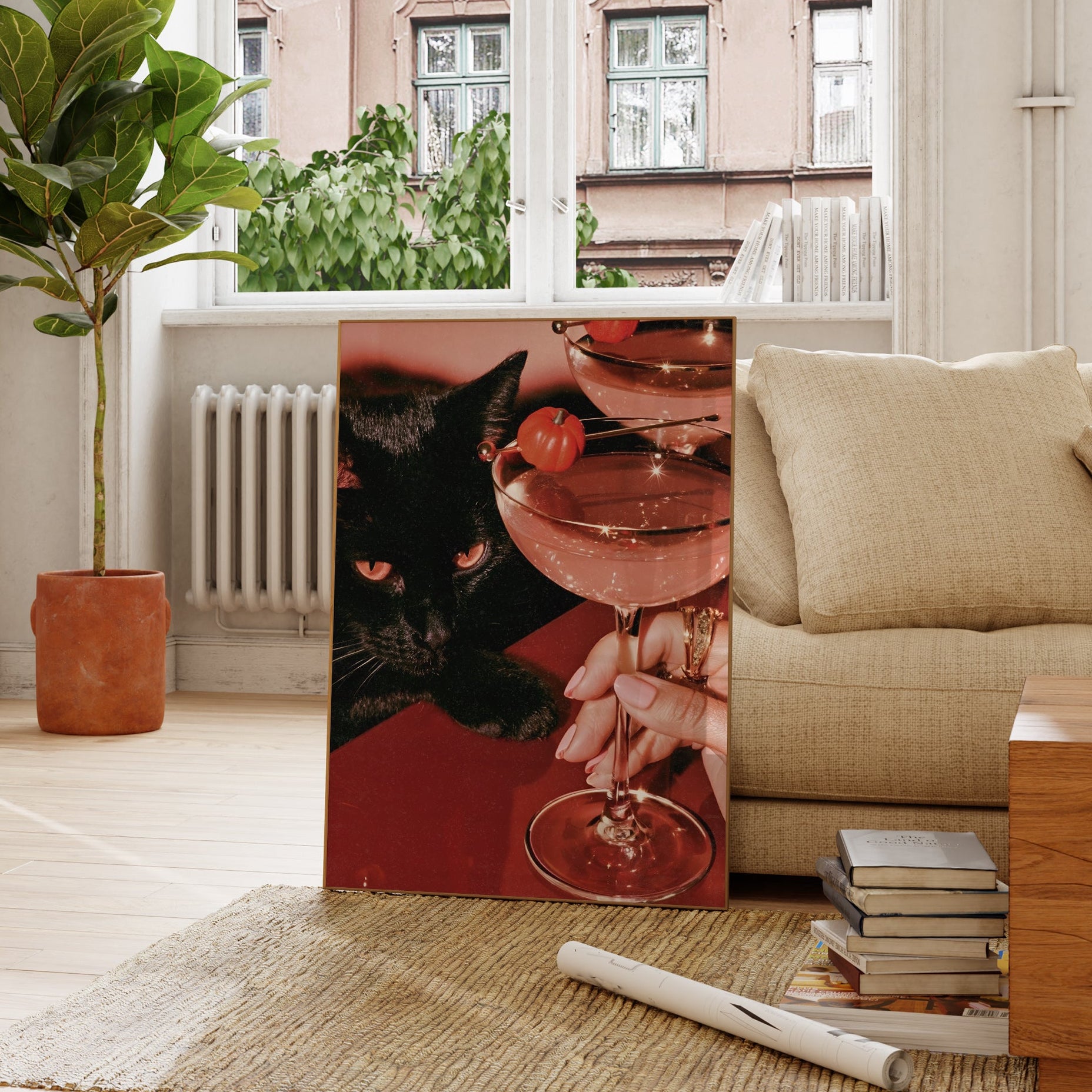 Vertical photographic print of a black cat with amber eyes resting beside two pink martini cocktails garnished with tiny orange pumpkins, on a deep red surface with a woman's hand holding one glass stem.