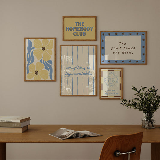 Set of five prints in butter yellow and blue: "The Homebody Club," a floral illustration, "everything is figureoutable," "The good times are here" with stars, and "you are my sunshine" with a sun