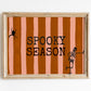 Horizontal print with orange and pink hand-painted vertical stripes, the words "SPOOKY SEASON" in bold black typewriter-style letters, a hanging black spider on the left, and a dancing skeleton illustration on the right.