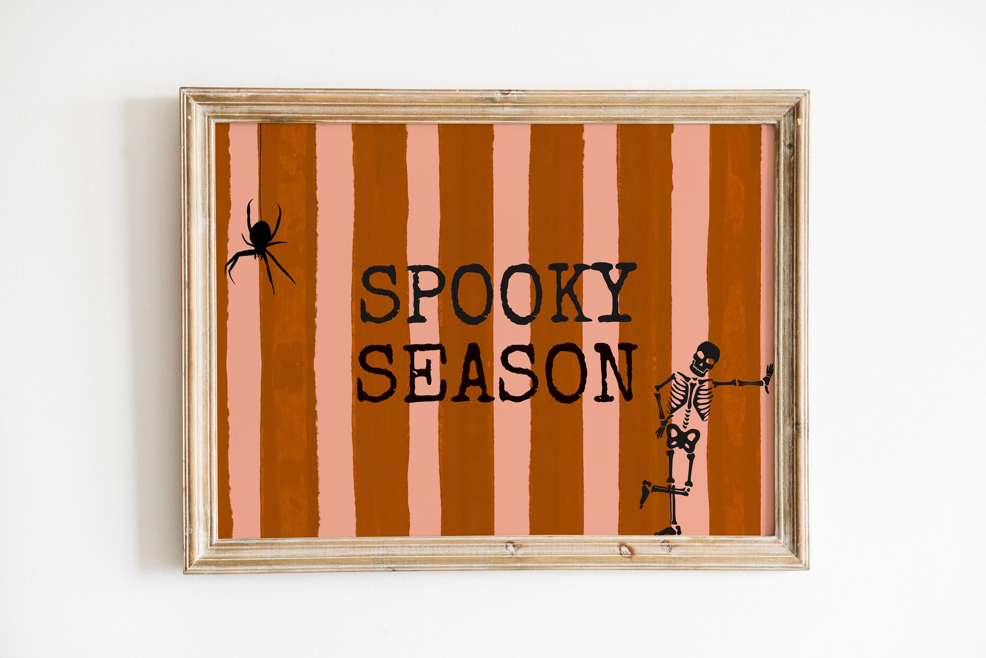 Horizontal print with orange and pink hand-painted vertical stripes, the words "SPOOKY SEASON" in bold black typewriter-style letters, a hanging black spider on the left, and a dancing skeleton illustration on the right.