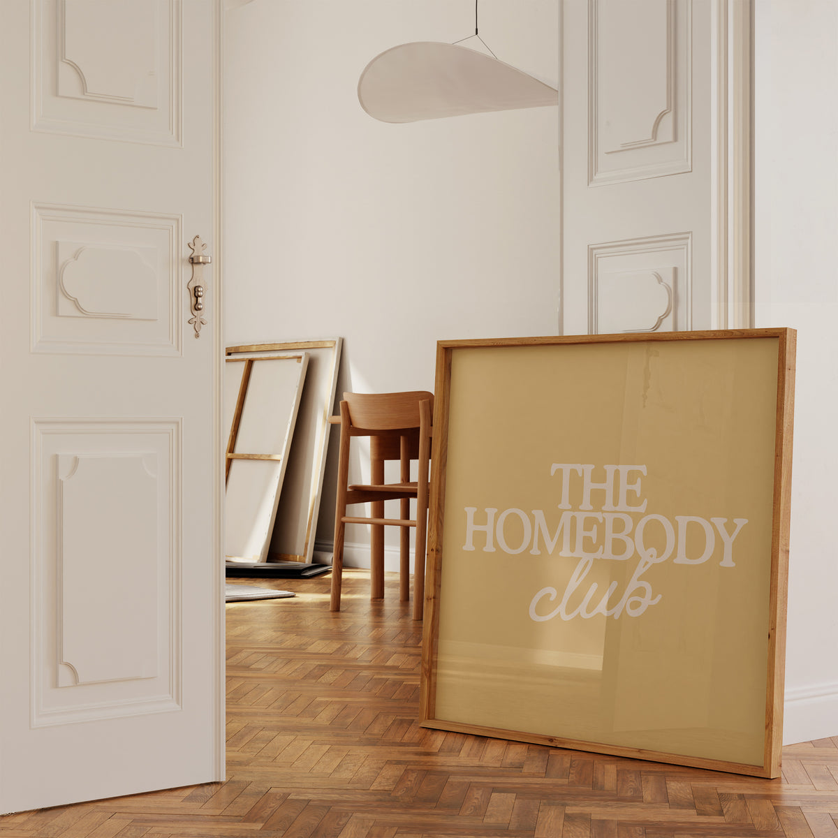 Square digital print with a mustard yellow background featuring "THE HOMEBODY" in bold cream serif type stacked above "club" in cream cursive script, centered typography layout.