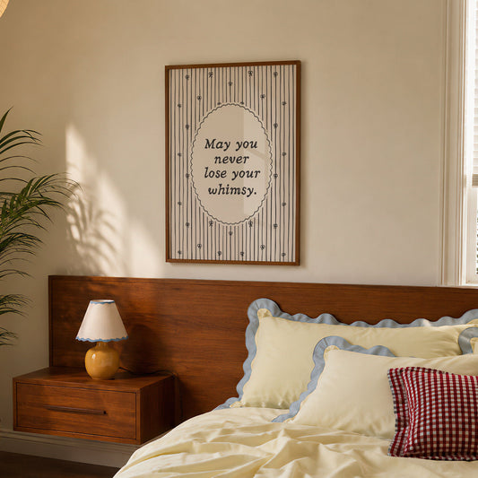 Vertical print with the quote "May you never lose your whimsy." in italic serif type inside a scalloped oval frame, surrounded by thin navy pinstripes decorated with small hand-drawn bows on a cream background.