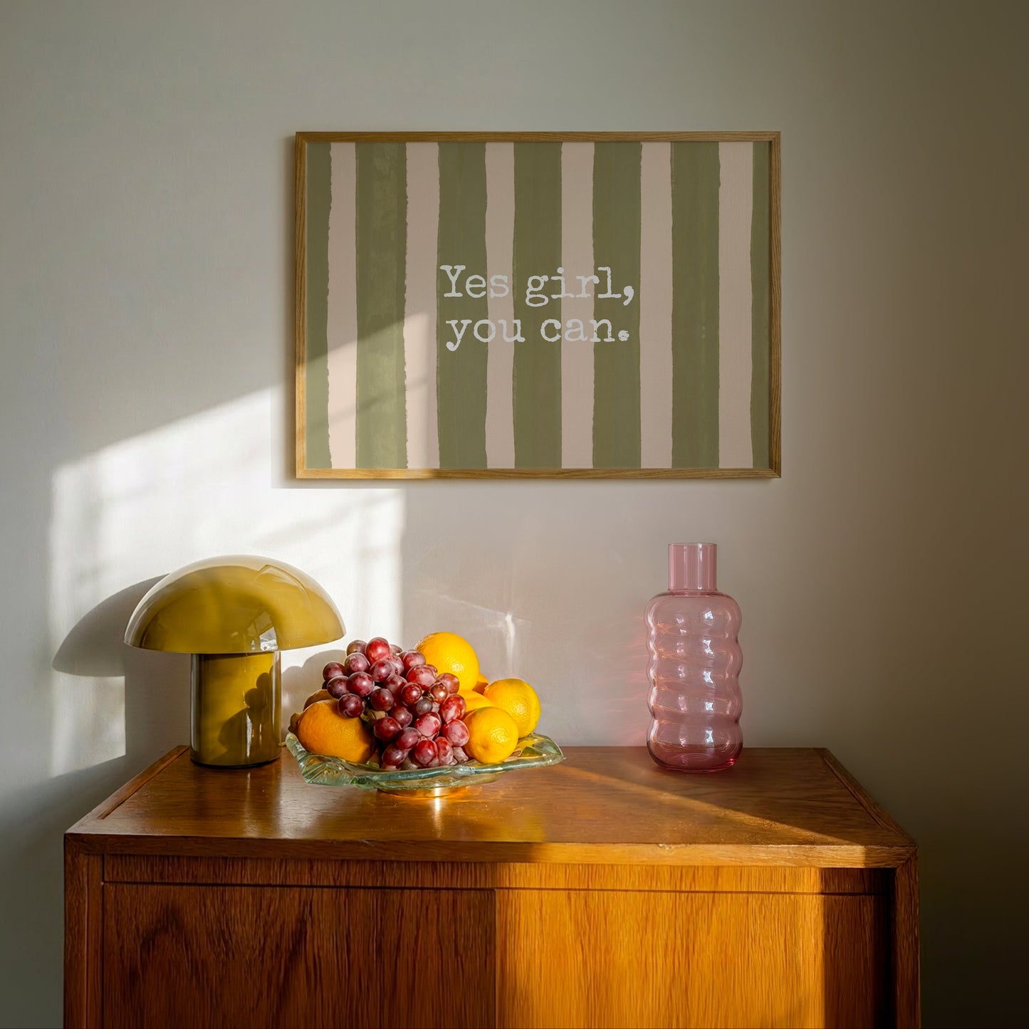 Horizontal wall print with bold olive green brush stroke vertical stripes on a warm cream background with white typewriter font text reading Yes girl, you can.