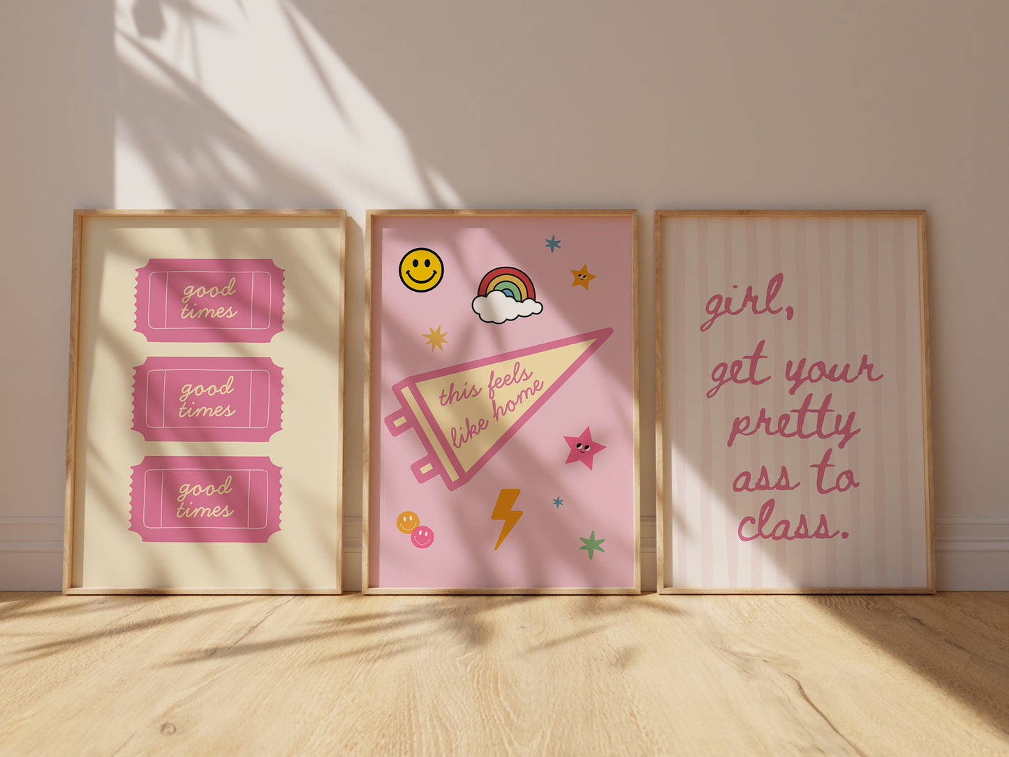 Three pink dorm art prints leaning against wall — Good Times tickets, This Feels Like Home pennant, Girl Get Your Pretty Ass To Class