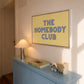 Set of five prints in butter yellow and blue: "The Homebody Club," a floral illustration, "everything is figureoutable," "The good times are here" with stars, and "you are my sunshine" with a sun