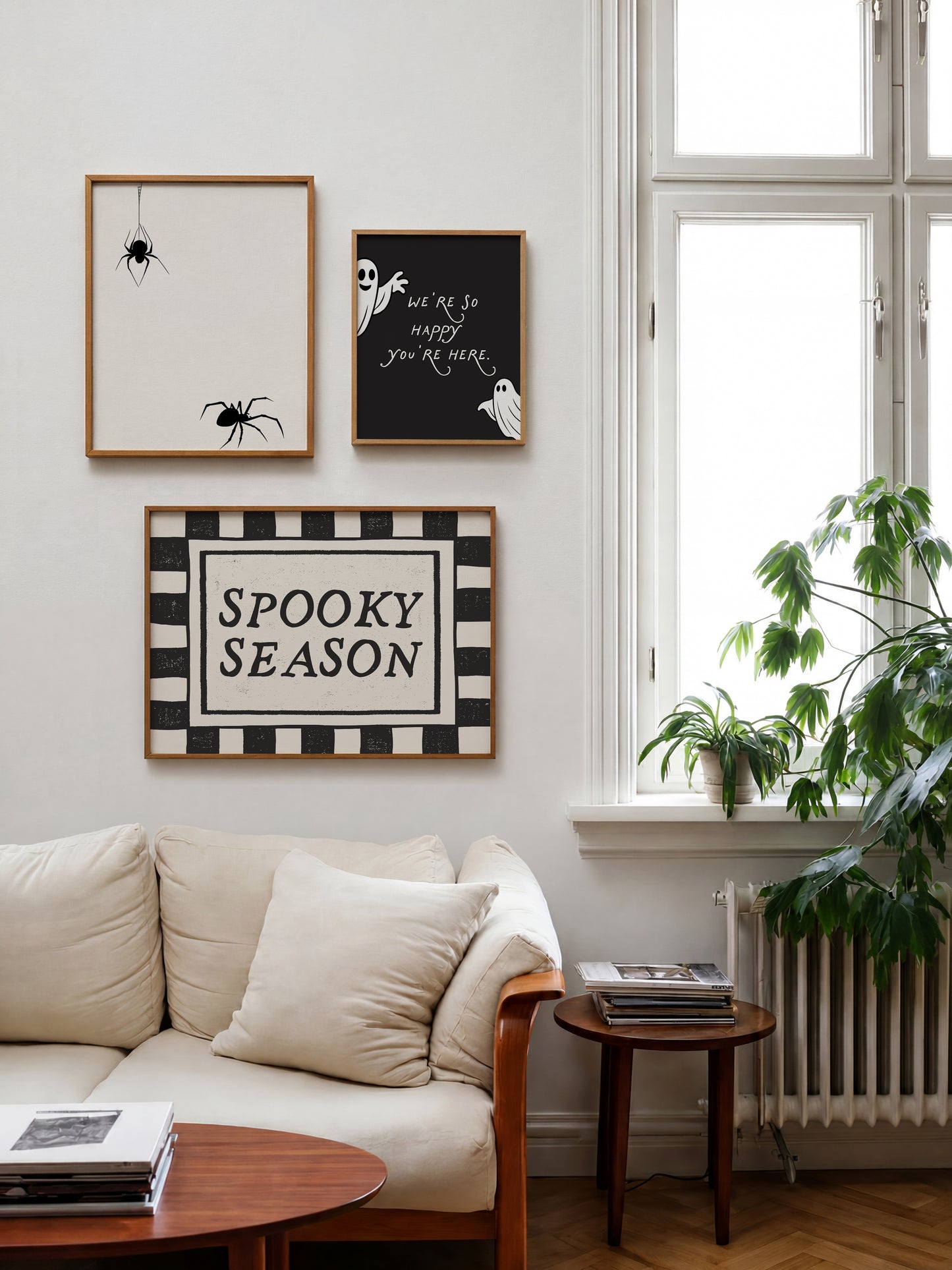 Set of 3 Halloween prints: a black background print with cartoon ghosts reading "We're so happy you're here," a checkered "Spooky Season" print, and a minimalist black spider illustration on a cream background.
