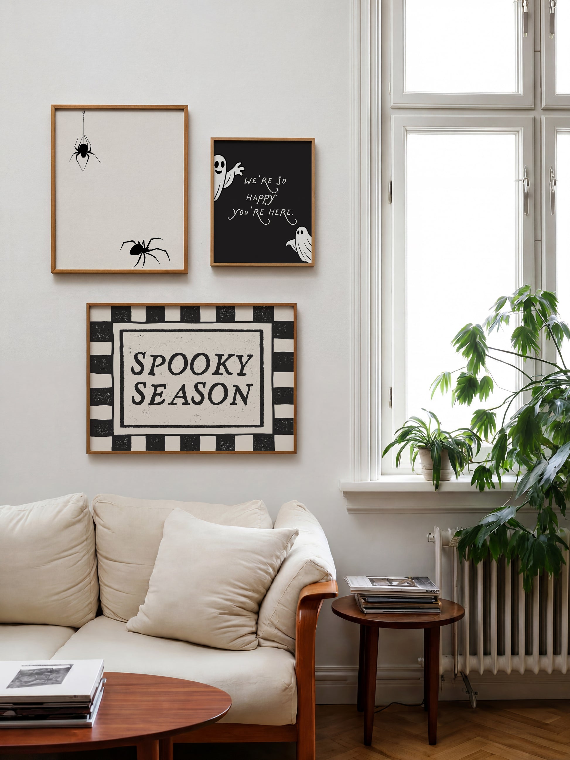 Set of 3 Halloween prints: a black background print with cartoon ghosts reading "We're so happy you're here," a checkered "Spooky Season" print, and a minimalist black spider illustration on a cream background.