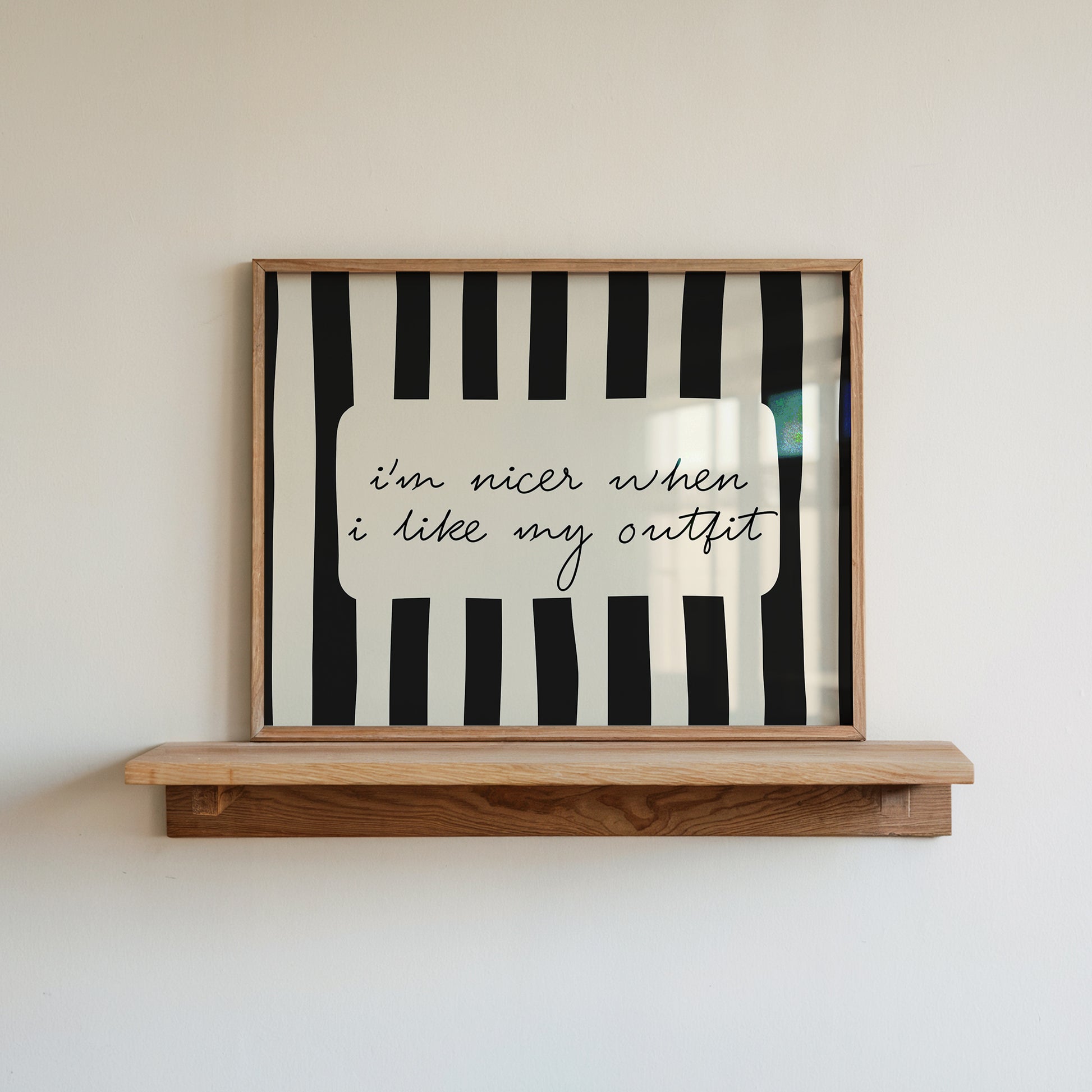 Horizontal print with bold black and white vertical stripes framing the handwritten cursive quote "i'm nicer when I like my outfit" in a rounded cream panel.
