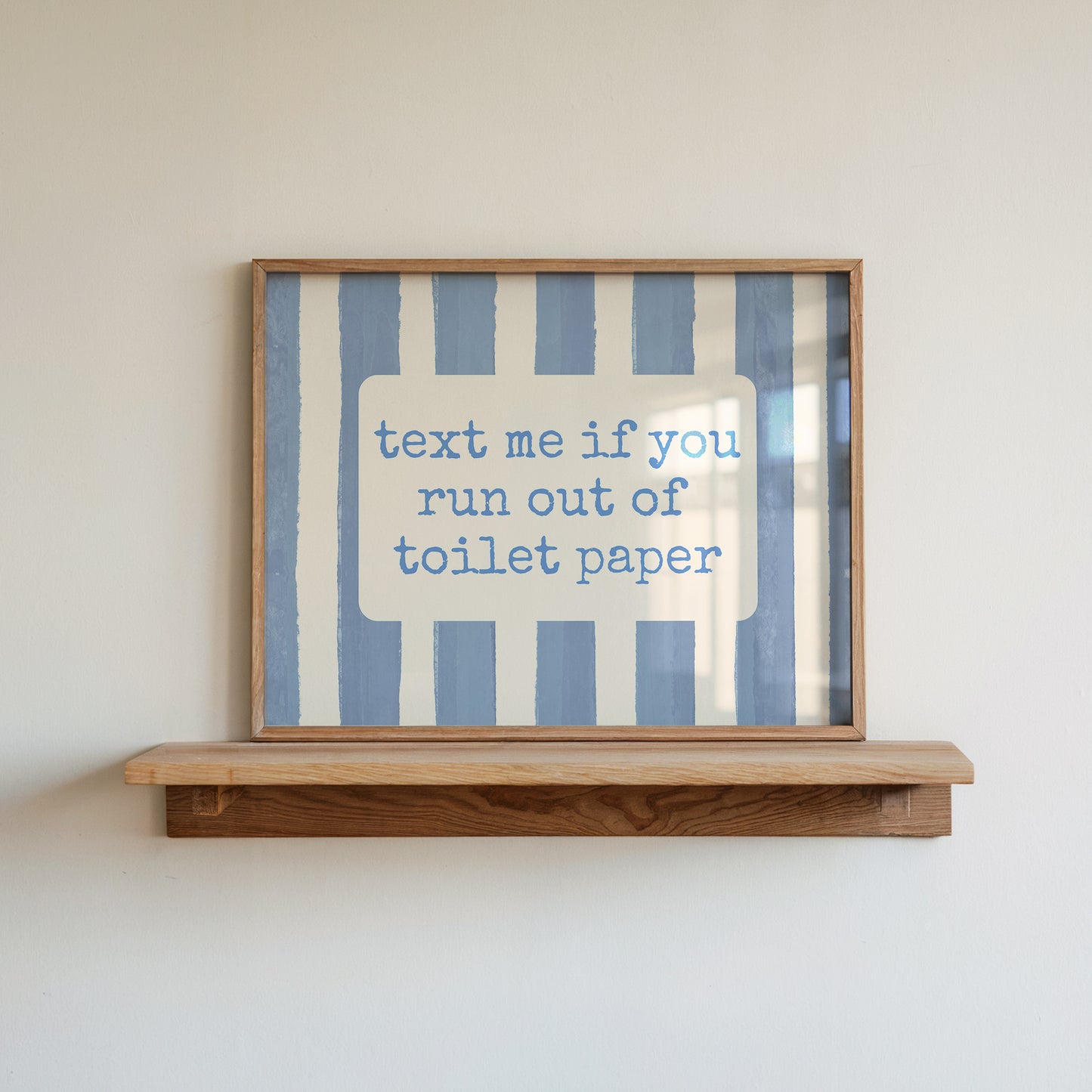 Horizontal wall print with dusty blue vertical brush stripes and a cream rounded text box in retro typewriter font reading text me if you run out of toilet paper