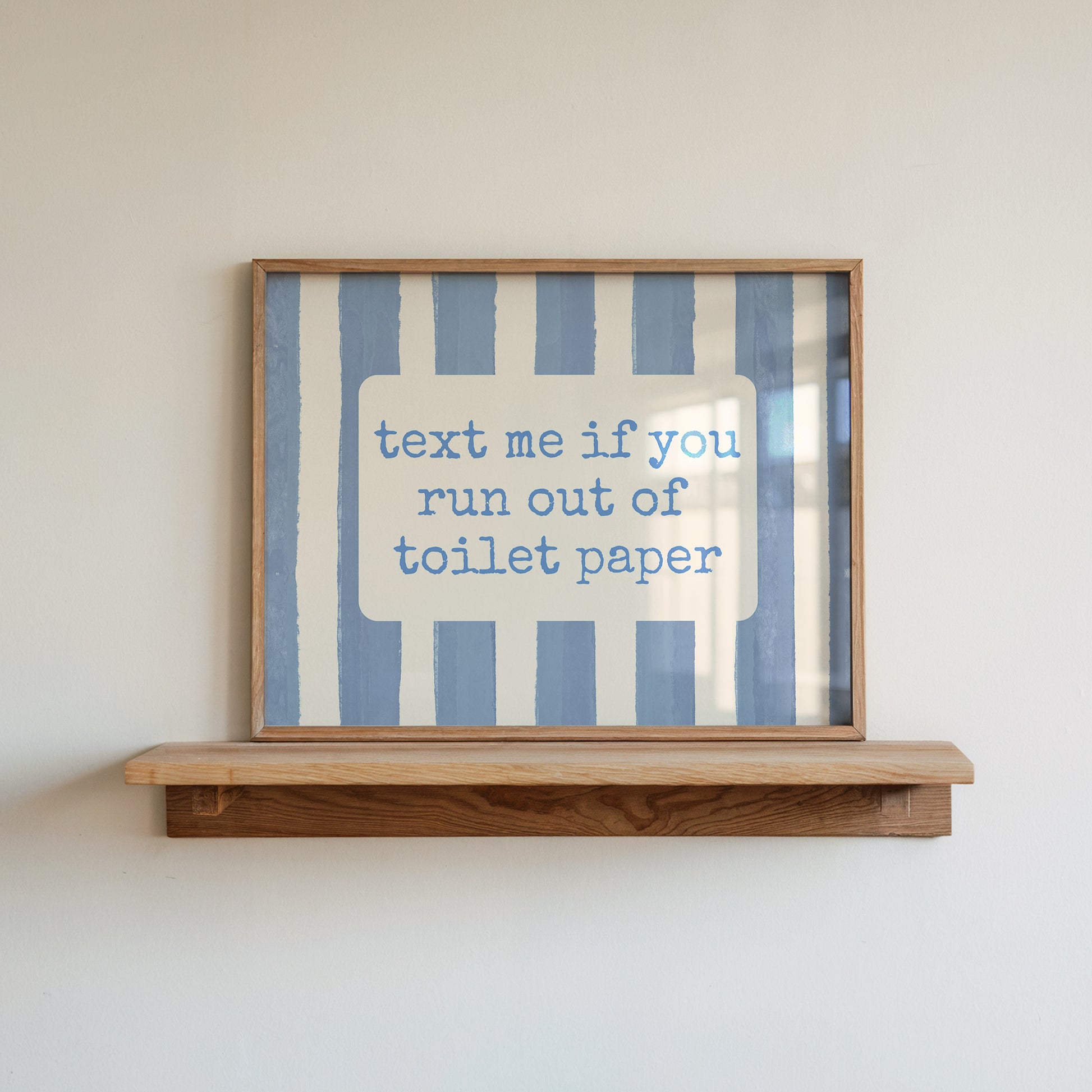 Horizontal wall print with dusty blue vertical brush stripes and a cream rounded text box in retro typewriter font reading text me if you run out of toilet paper