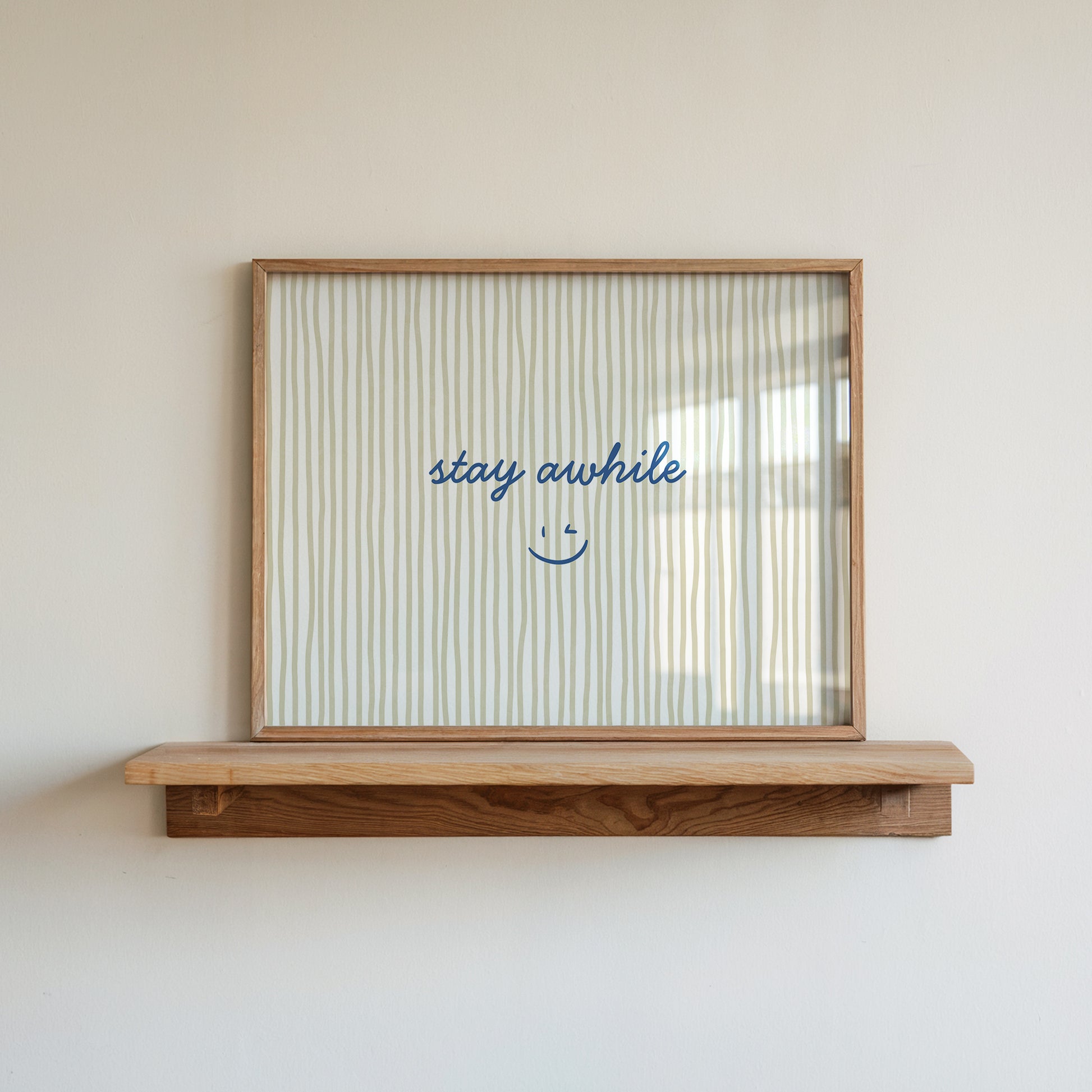 Horizontal print with thin hand-painted tan and cream vertical stripes, the quote "stay awhile" in navy cursive script, and a small hand-drawn smiley face beneath it.