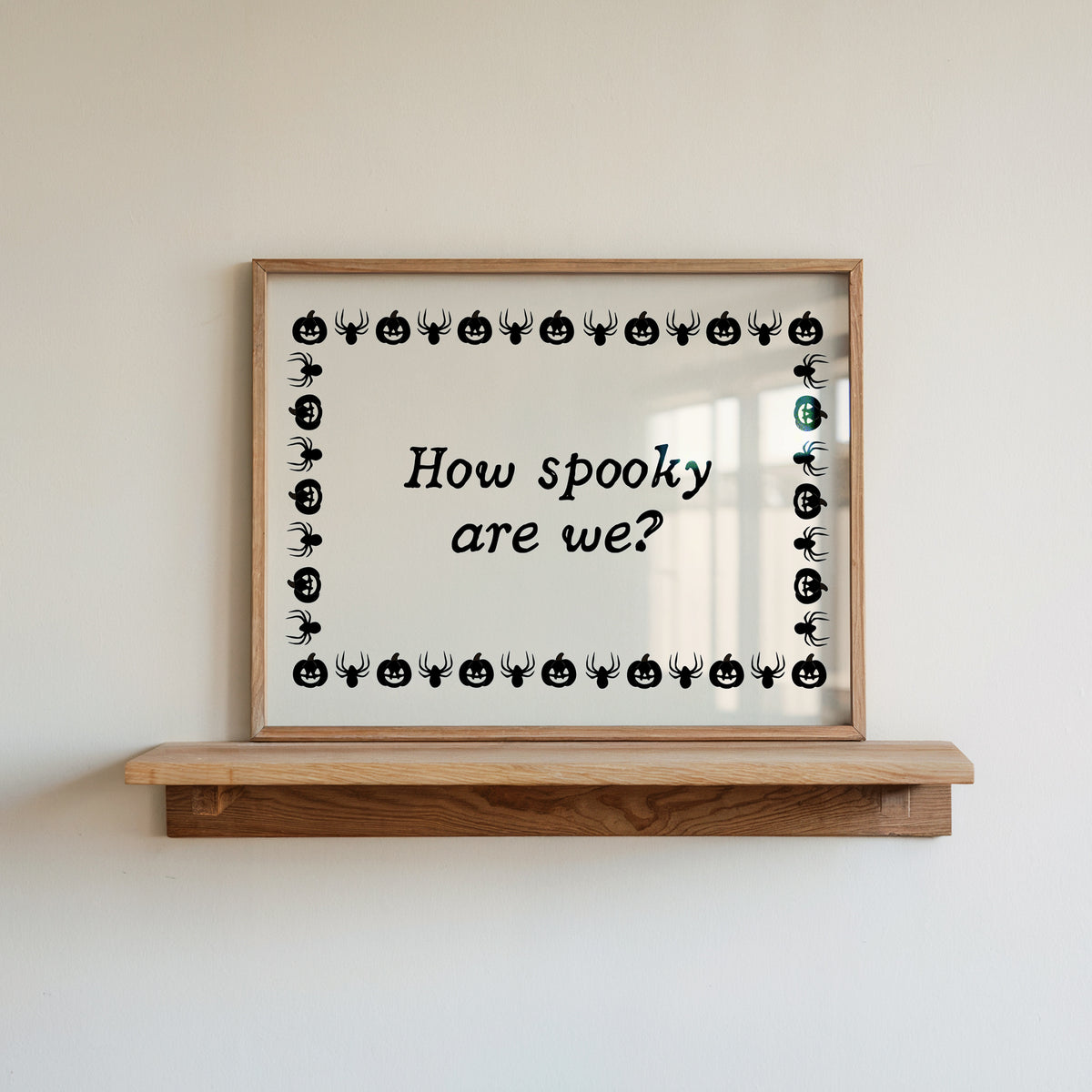 Landscape digital print with a cream background bordered by alternating black pumpkin and spider illustrations, framing the hand-lettered phrase "How spooky are we?" in black script.