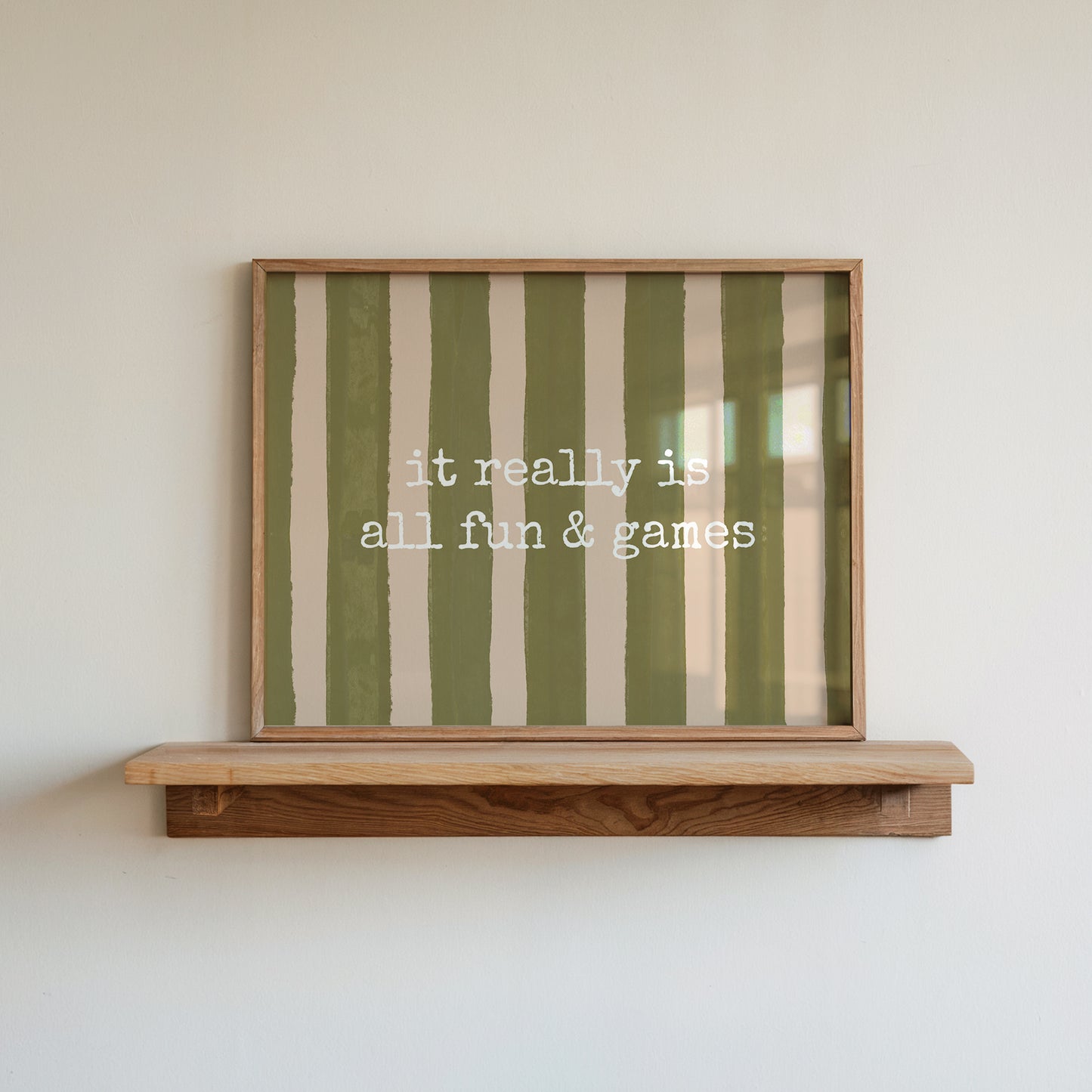 Horizontal print with olive green and cream hand-painted vertical stripes and the quote "it really is all fun & games" in white typewriter-style lettering across the center.