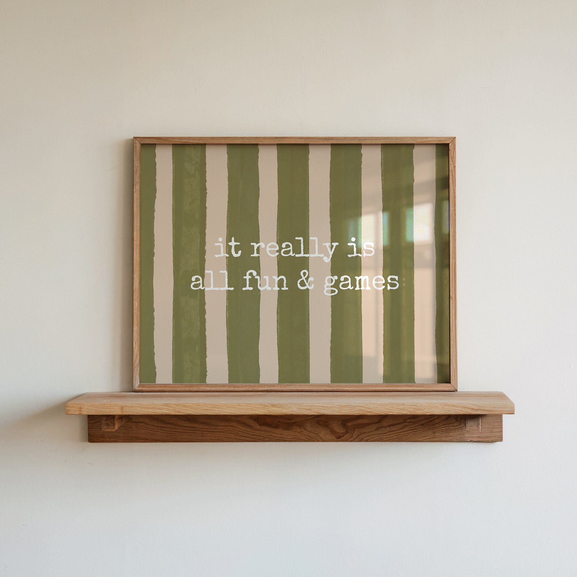 Horizontal print with olive green and cream hand-painted vertical stripes and the quote "it really is all fun & games" in white typewriter-style lettering across the center.