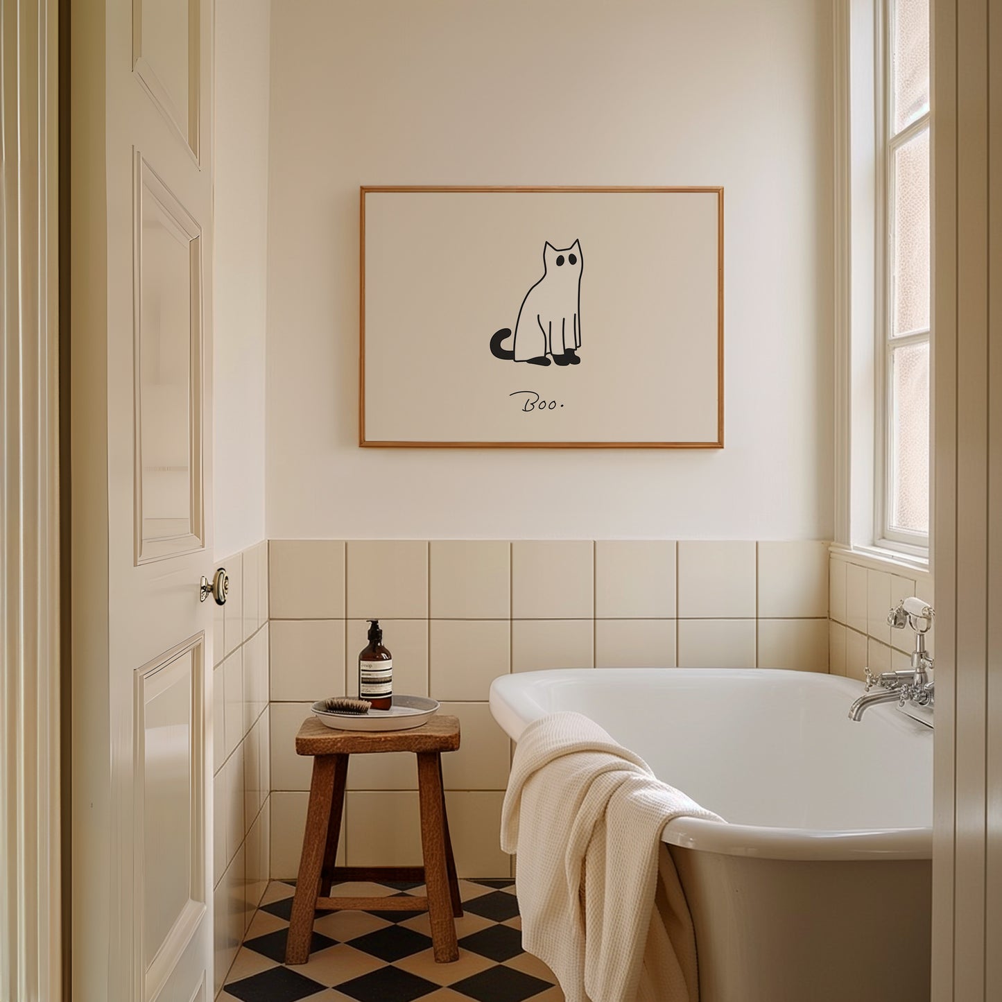 Horizontal minimalist print of a black cat wearing a white ghost sheet costume with cut-out eyes, sitting beside the handwritten word "Boo." on a cream background.