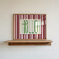 Horizontal wall print with bold dark red vertical stripes and a green dotted border text box reading HELLO! in chunky rounded green font