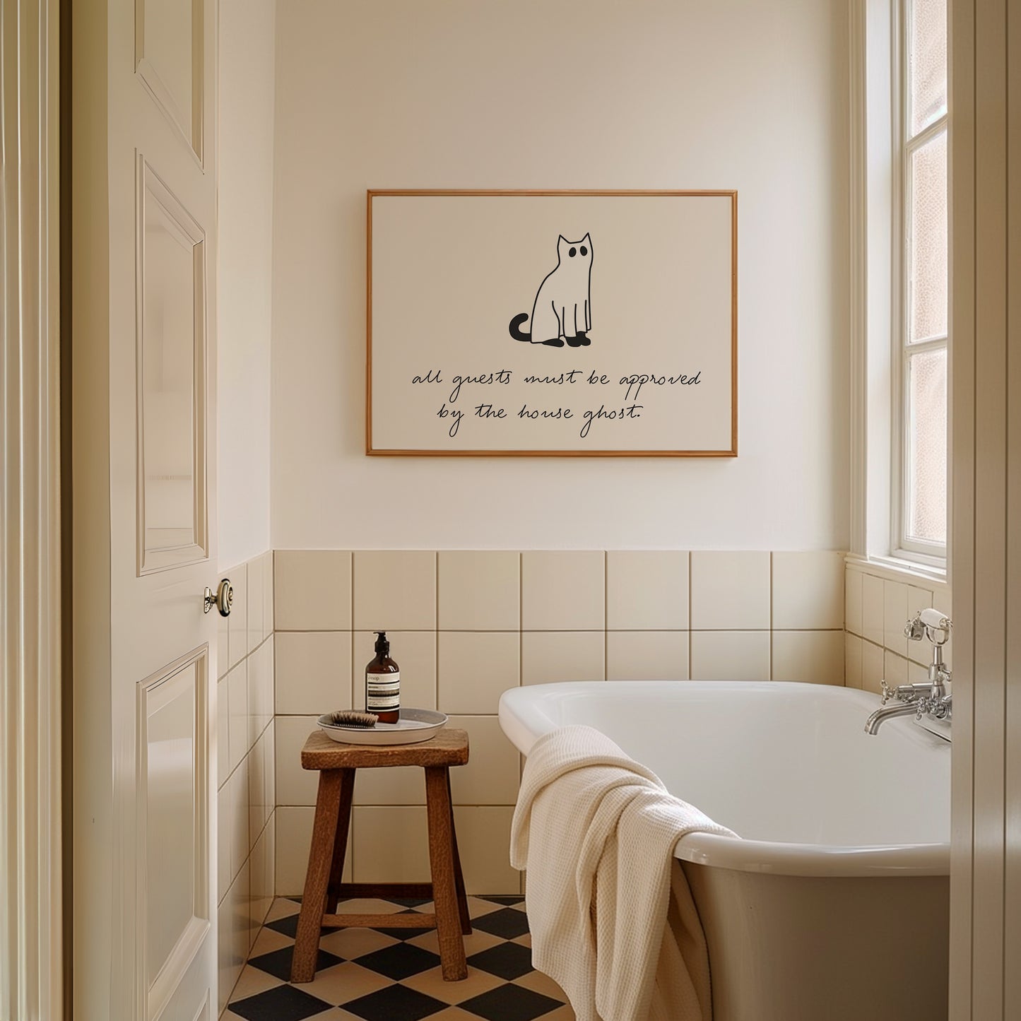 Horizontal minimalist Halloween print of a black cat wearing a white ghost sheet costume with cut-out eyes, above the handwritten cursive quote "all guests must be approved by the house ghost." on a cream background.