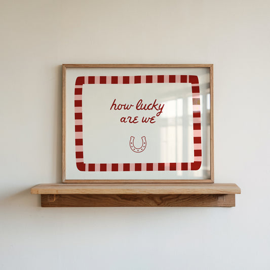 White print with a red and pink striped border featuring the handwritten quote 'how lucky are we' and a horseshoe illustration