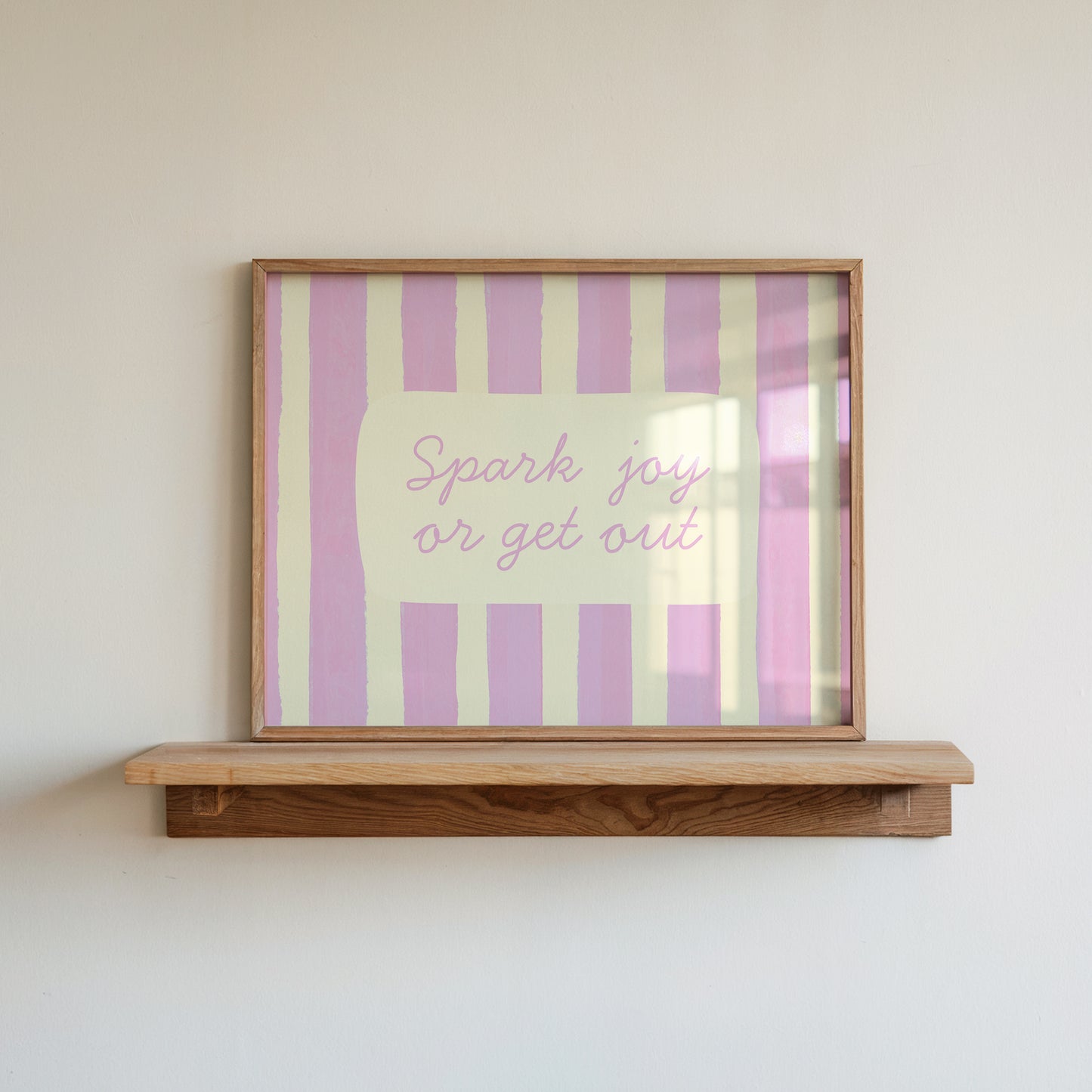 Horizontal art print with hand-painted pink and cream vertical stripes and the quote "Spark joy or get out" in pink cursive script inside a rounded cream panel at the centre.