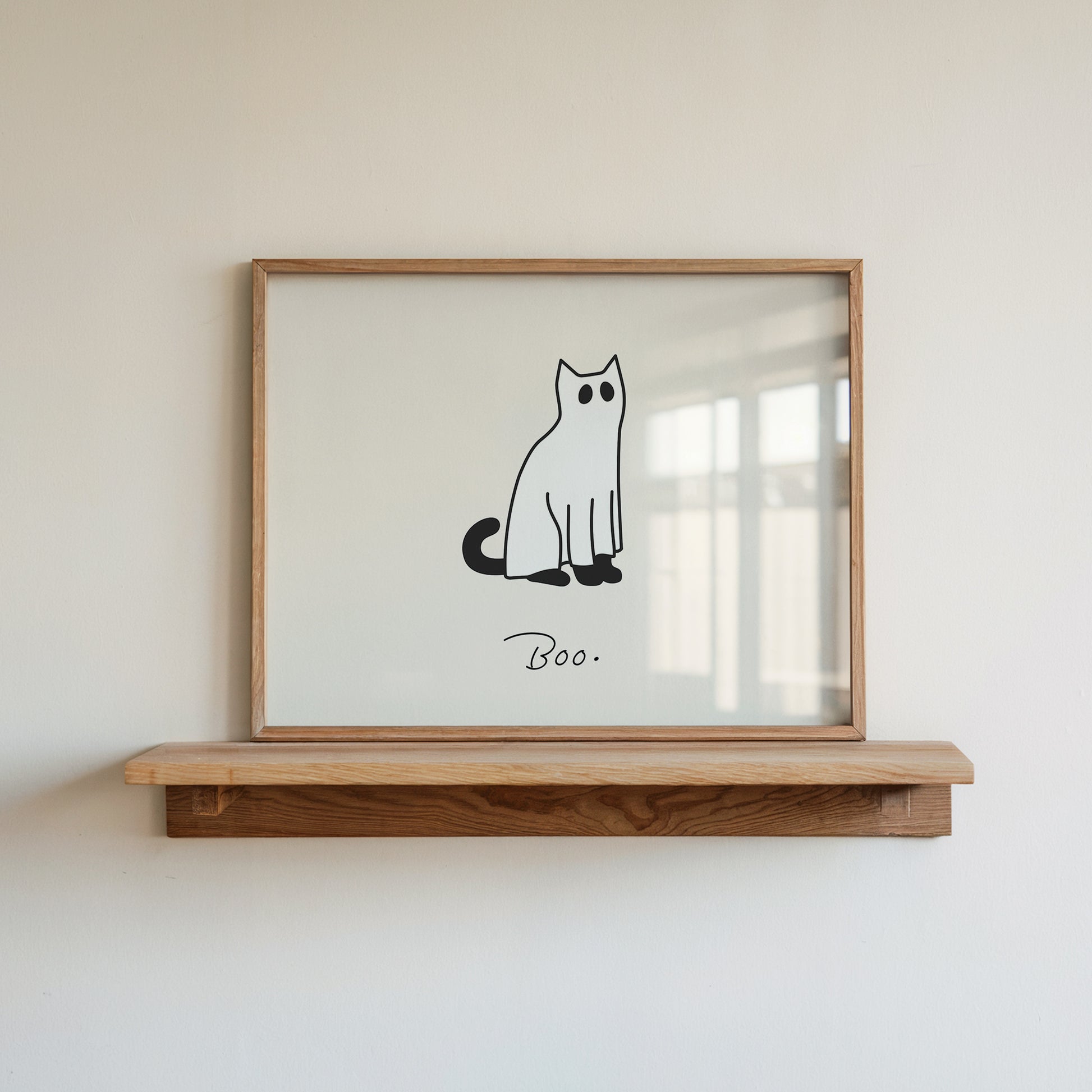 Horizontal minimalist print of a black cat wearing a white ghost sheet costume with cut-out eyes, sitting beside the handwritten word "Boo." on a cream background.