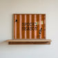 Horizontal print with orange and pink hand-painted vertical stripes, the words "SPOOKY SEASON" in bold black typewriter-style letters, a hanging black spider on the left, and a dancing skeleton illustration on the right.