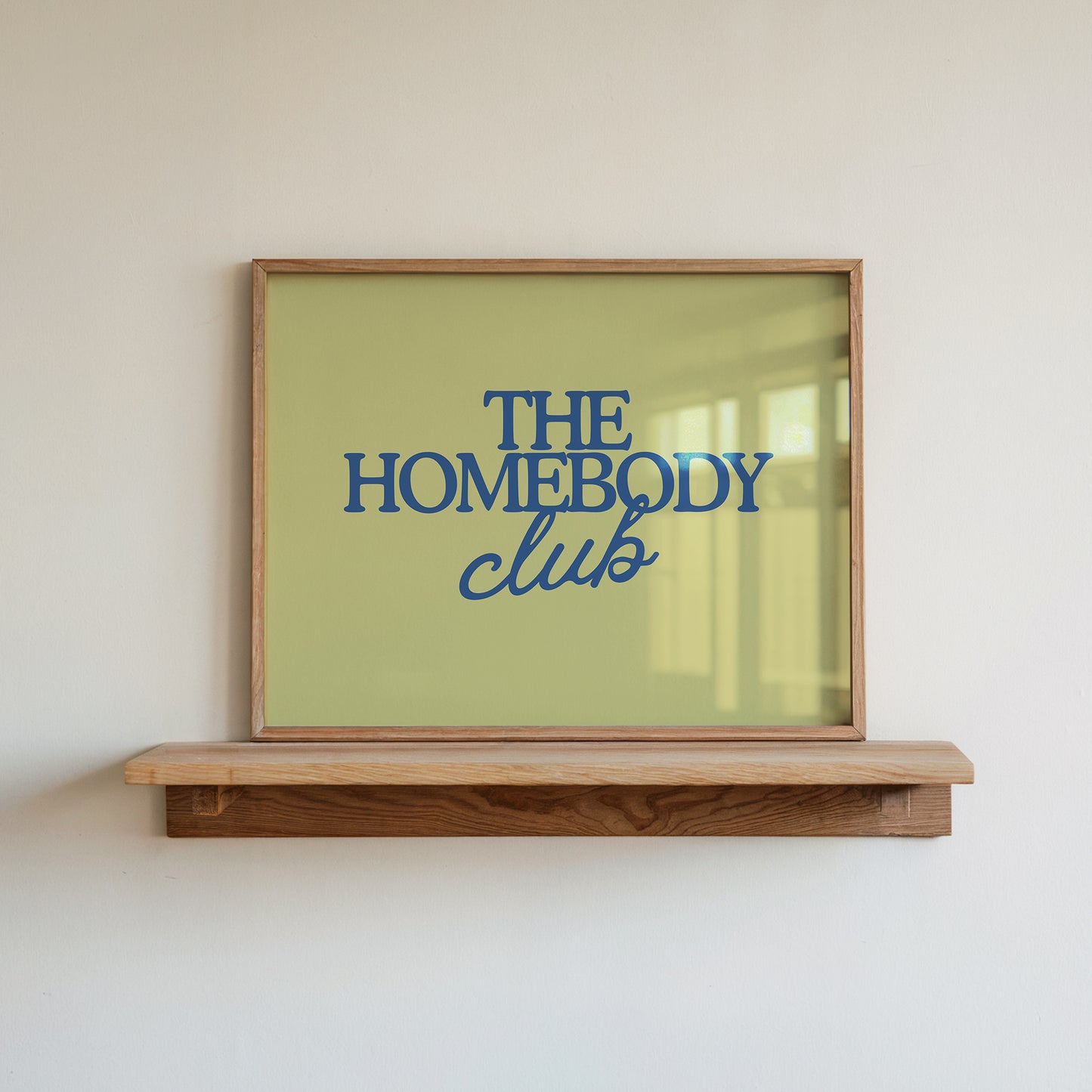 Rectangular landscape digital print with an olive-green background featuring "THE HOMEBODY" in bold blue serif type stacked above "club" in blue cursive script, centered typography layout.
