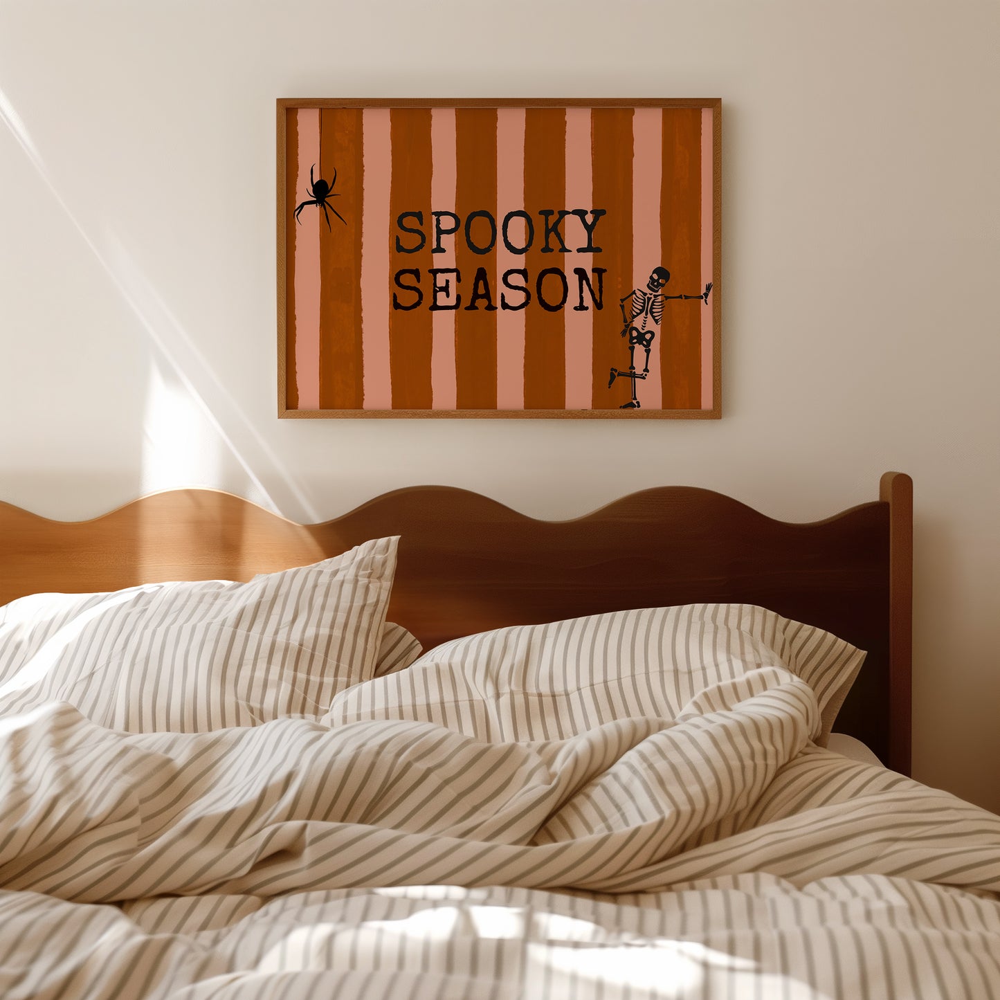 Horizontal print with orange and pink hand-painted vertical stripes, the words "SPOOKY SEASON" in bold black typewriter-style letters, a hanging black spider on the left, and a dancing skeleton illustration on the right.