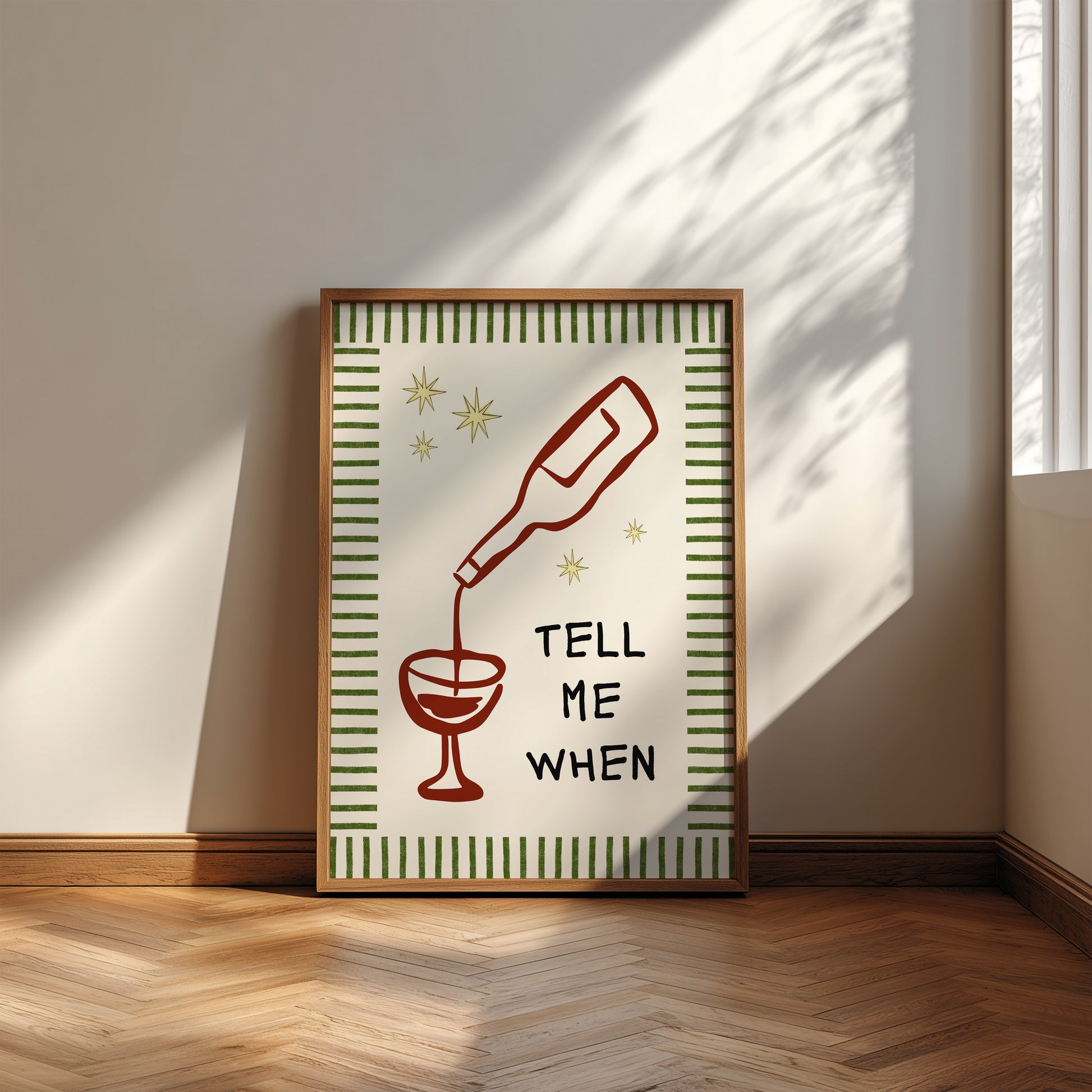 Vertical cream wall print with green stripe border, gold star details, and bold black typography reading Tell Me When alongside dark red hand-drawn line art of a wine bottle pouring into a glass