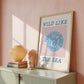 Set of 10 coastal watercolor prints in pink and blue: "Wild Like the Sea" beside a spiral shell illustration, "Stay Wild Ocean Child" in bold blue lettering, "Sea La Vie" in pink stamped typography, a mermaid lounging in a martini glass, pink starfish and seashell illustrations, a woman in a shell headdress, a beach umbrella watercolor, and "Meet me by the sea" in postcard-style script.