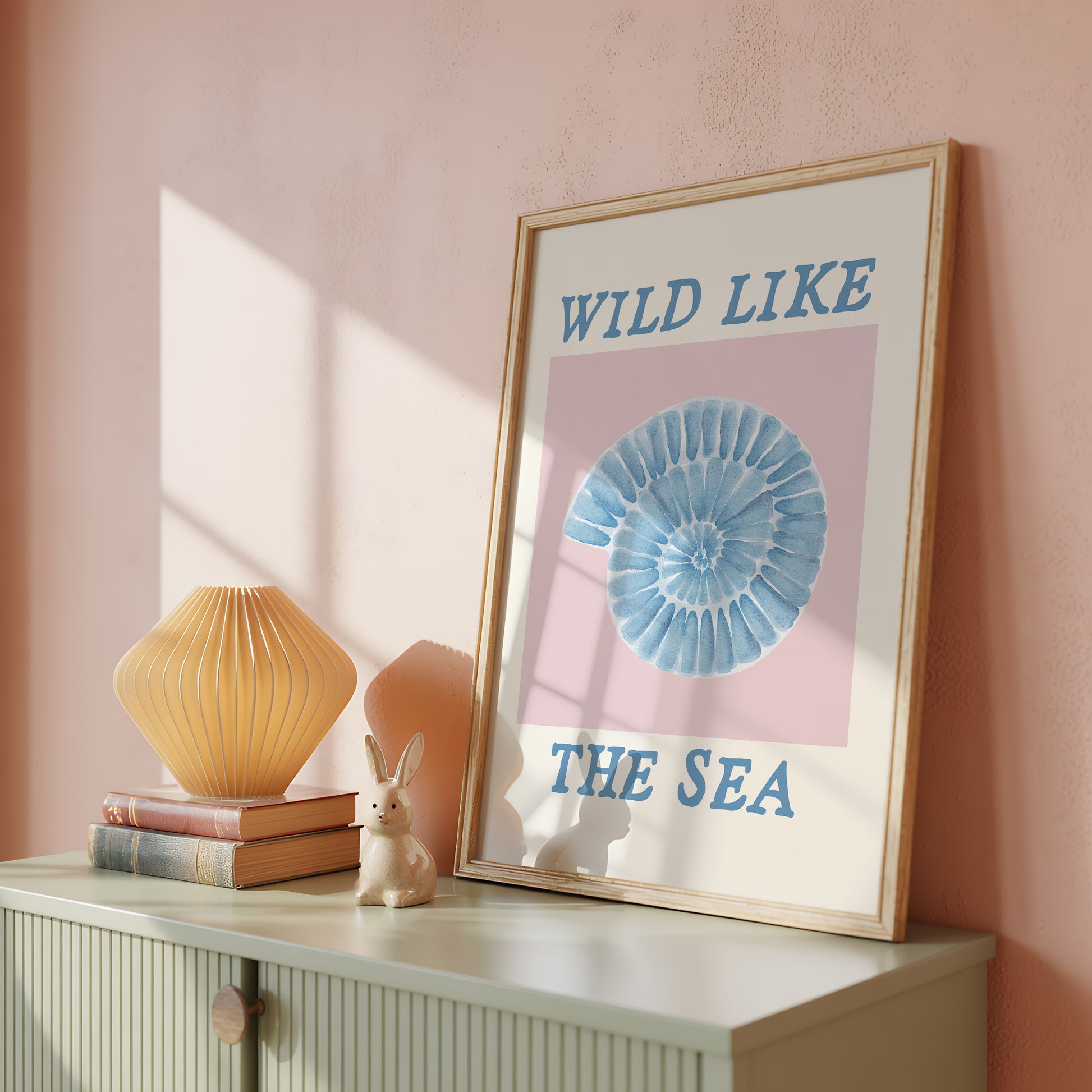 Set of 10 coastal watercolor prints in pink and blue: "Wild Like the Sea" beside a spiral shell illustration, "Stay Wild Ocean Child" in bold blue lettering, "Sea La Vie" in pink stamped typography, a mermaid lounging in a martini glass, pink starfish and seashell illustrations, a woman in a shell headdress, a beach umbrella watercolor, and "Meet me by the sea" in postcard-style script.