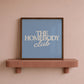 Square digital print with a dusty blue background featuring "THE HOMEBODY" in bold cream serif type stacked above "club" in cream cursive script, centered typography layout.