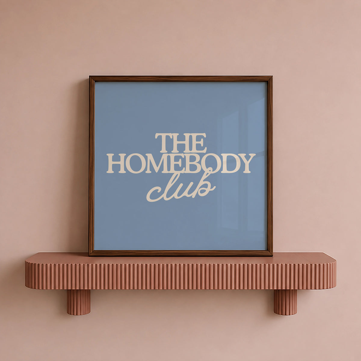 Square digital print with a dusty blue background featuring "THE HOMEBODY" in bold cream serif type stacked above "club" in cream cursive script, centered typography layout.